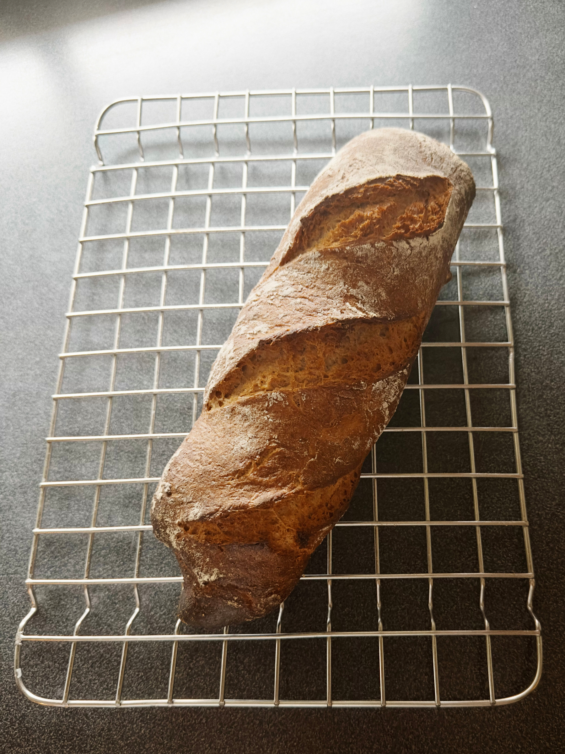 A loaf of rustic bread rests on a wire cooling rack.