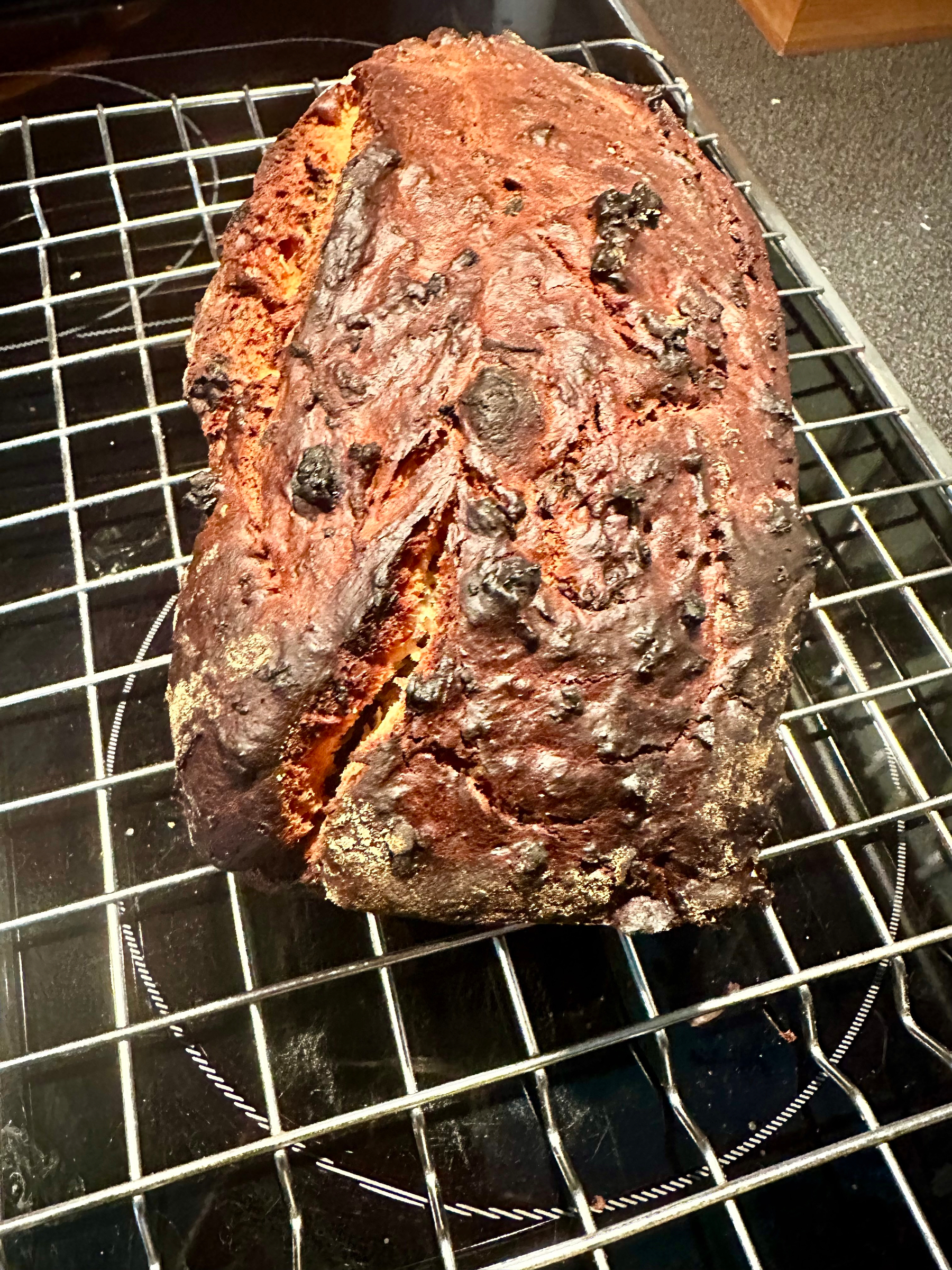 A loaf of bread appears overcooked and burnt on a cooling rack.