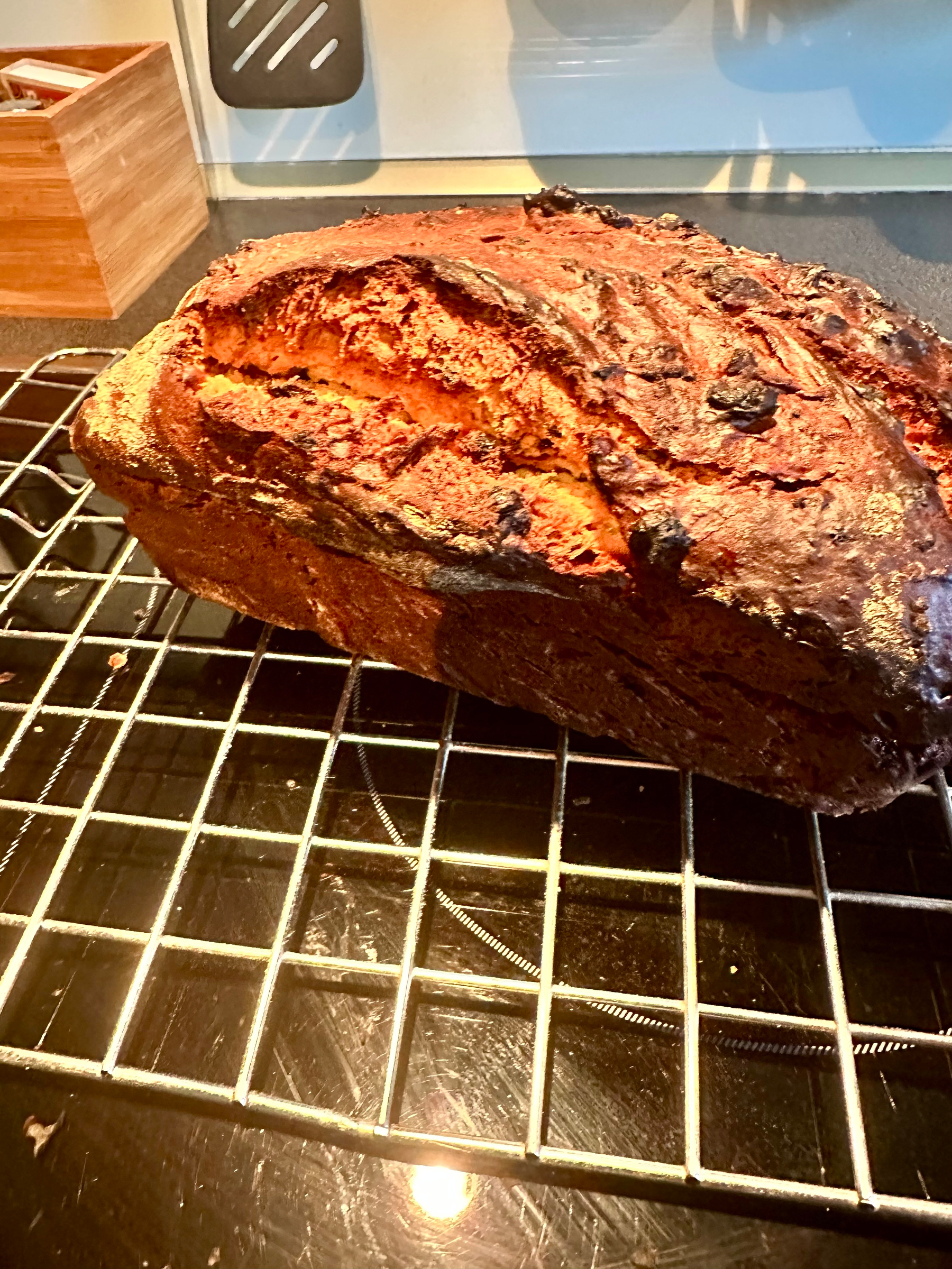 A freshly baked loaf of bread is cooling on a wire rack in a kitchen setting.