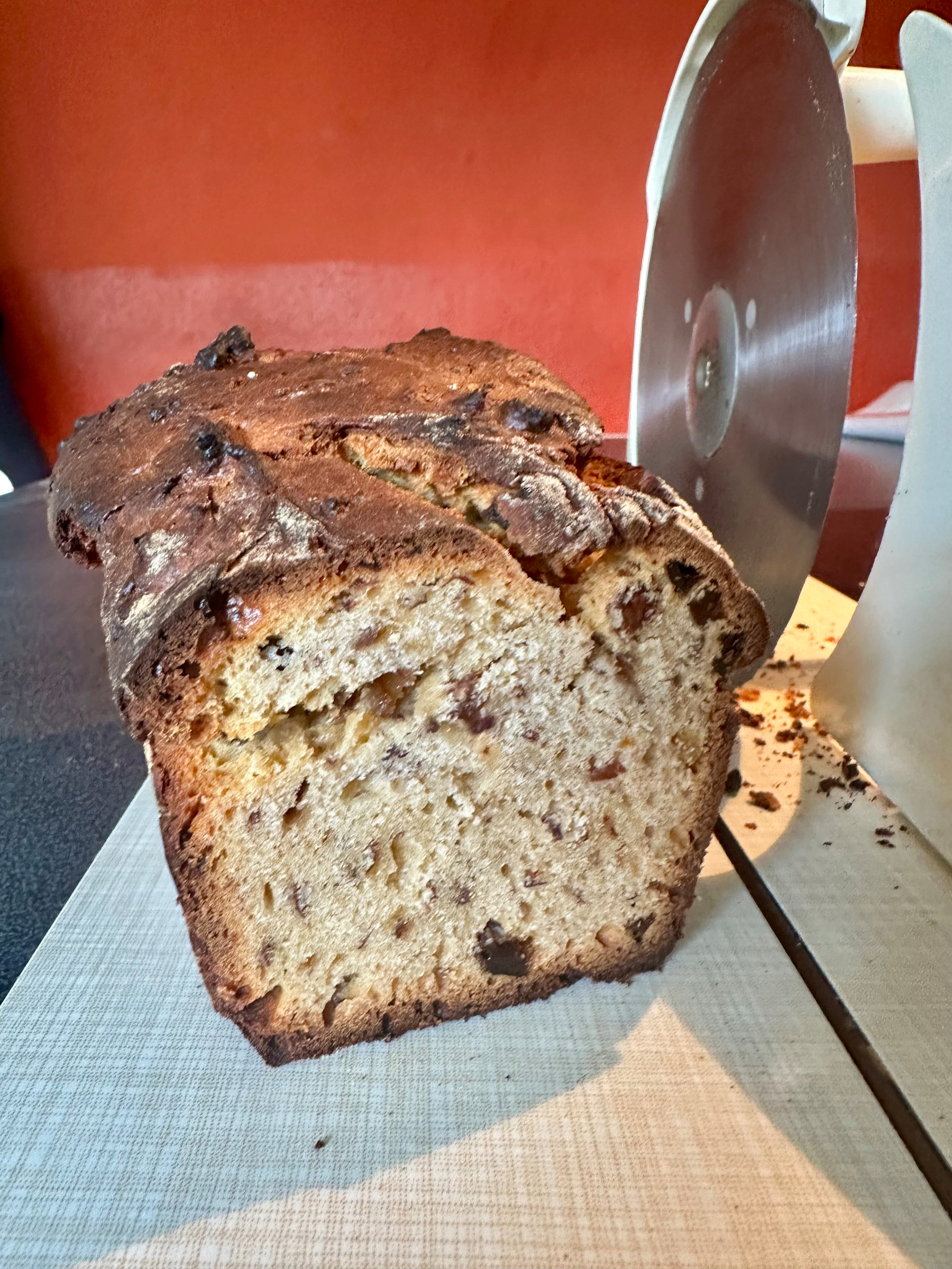 A freshly sliced loaf of fruit and nut bread sits on a cutting board next to a bread slicer.