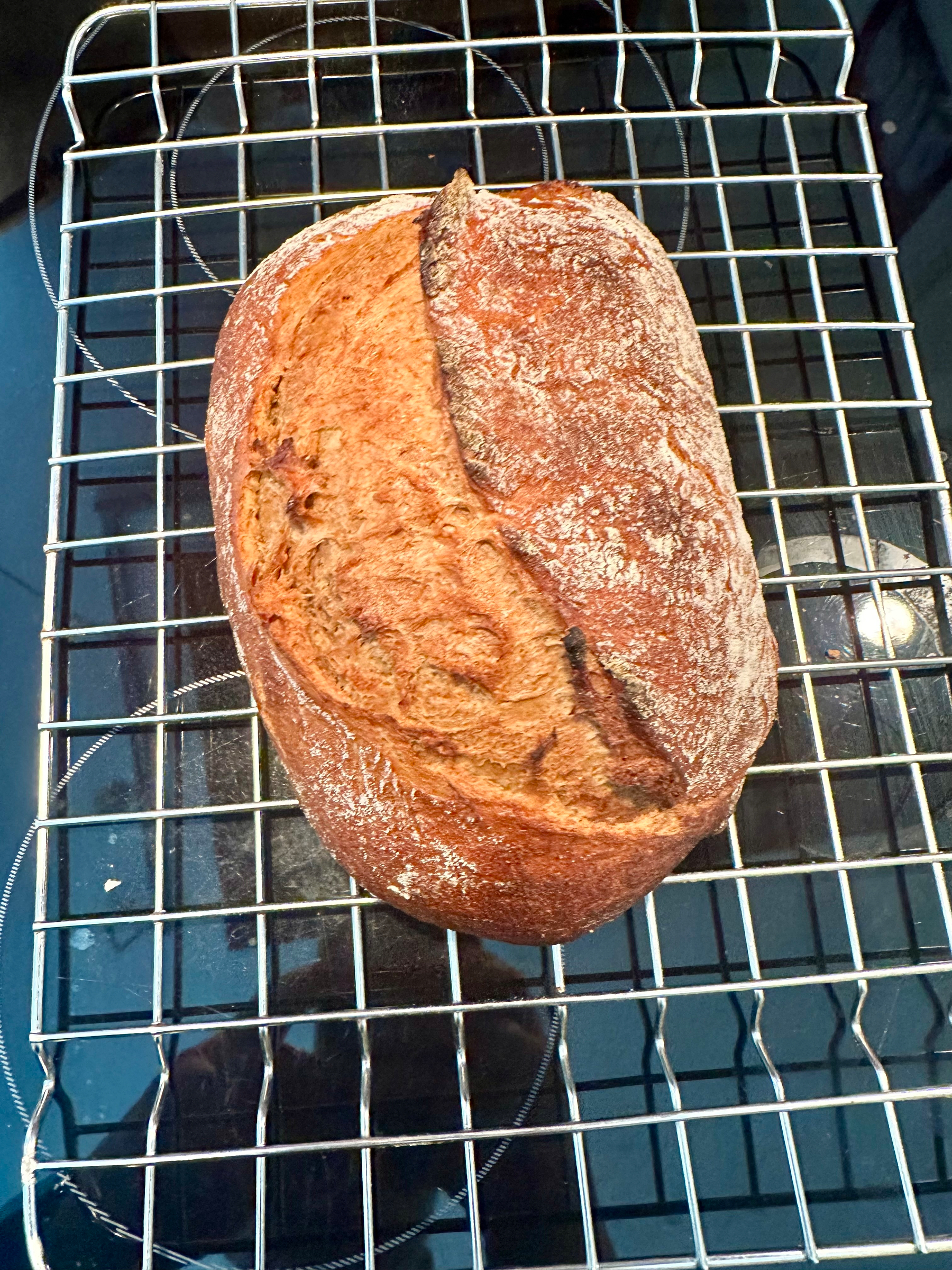 A freshly baked loaf of rustic bread rests on a wire cooling rack.