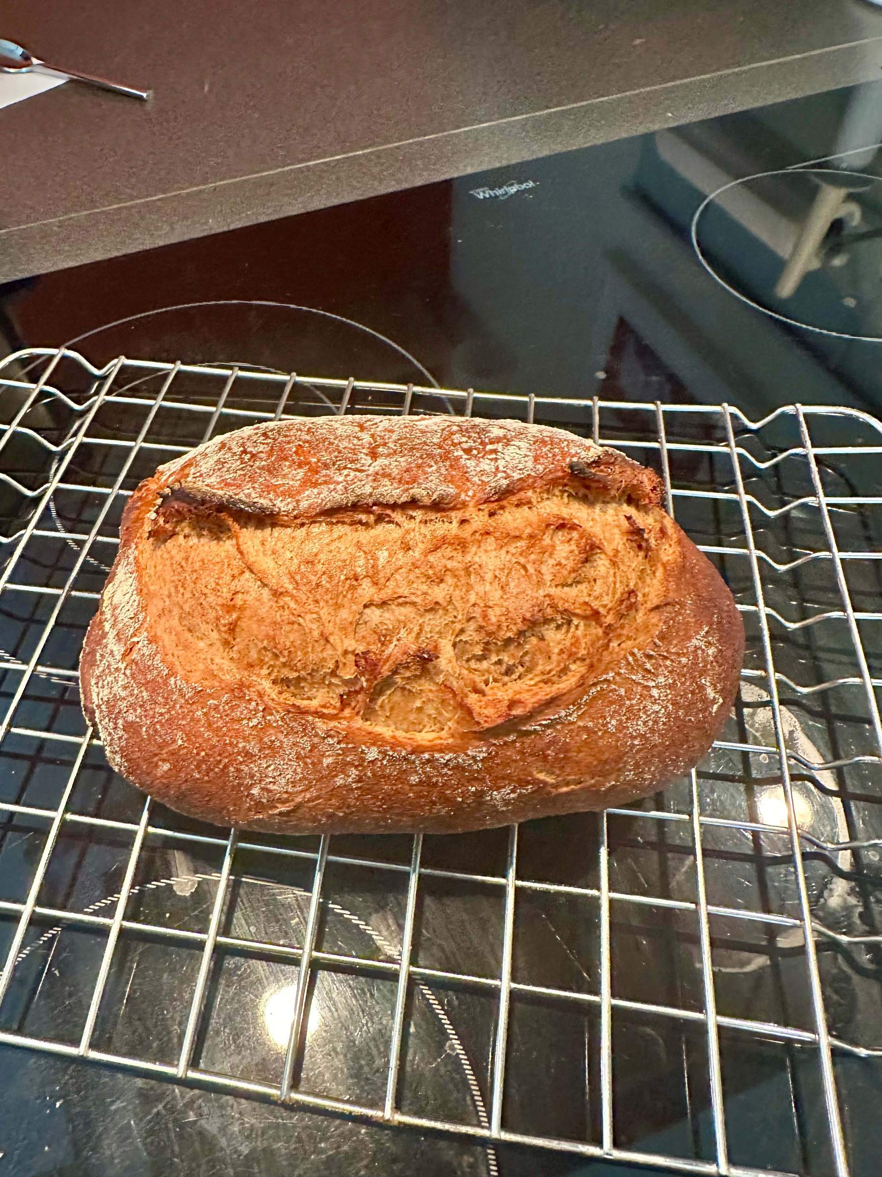 A freshly baked loaf of crusty bread is cooling on a wire rack placed over a stovetop.