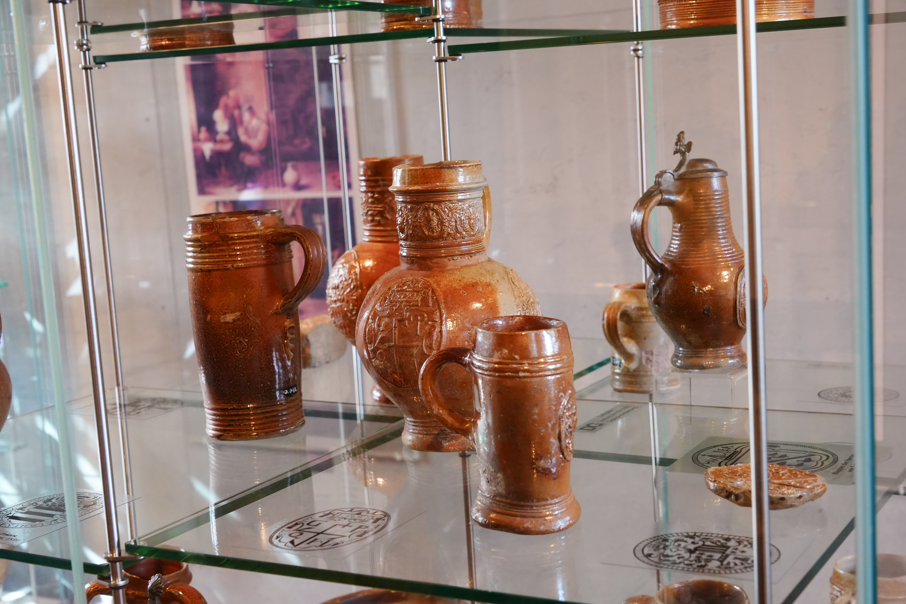 Several earthenware jugs and mugs are displayed on glass shelves in a cabinet.