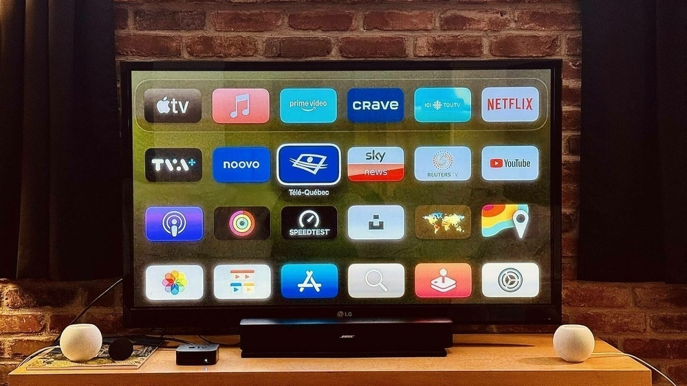 A television screen displays a selection of streaming and application icons, including Apple TV, Netflix, and YouTube, in a home setting with a brick wall background.