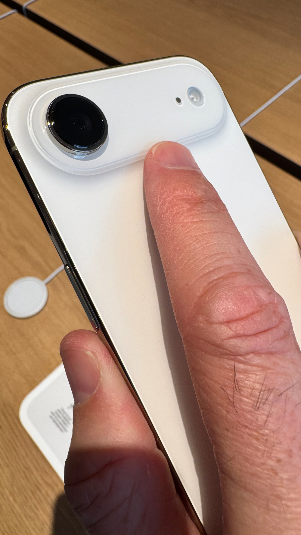 A person is holding a white smartphone, focusing on the camera area with their finger nearby.