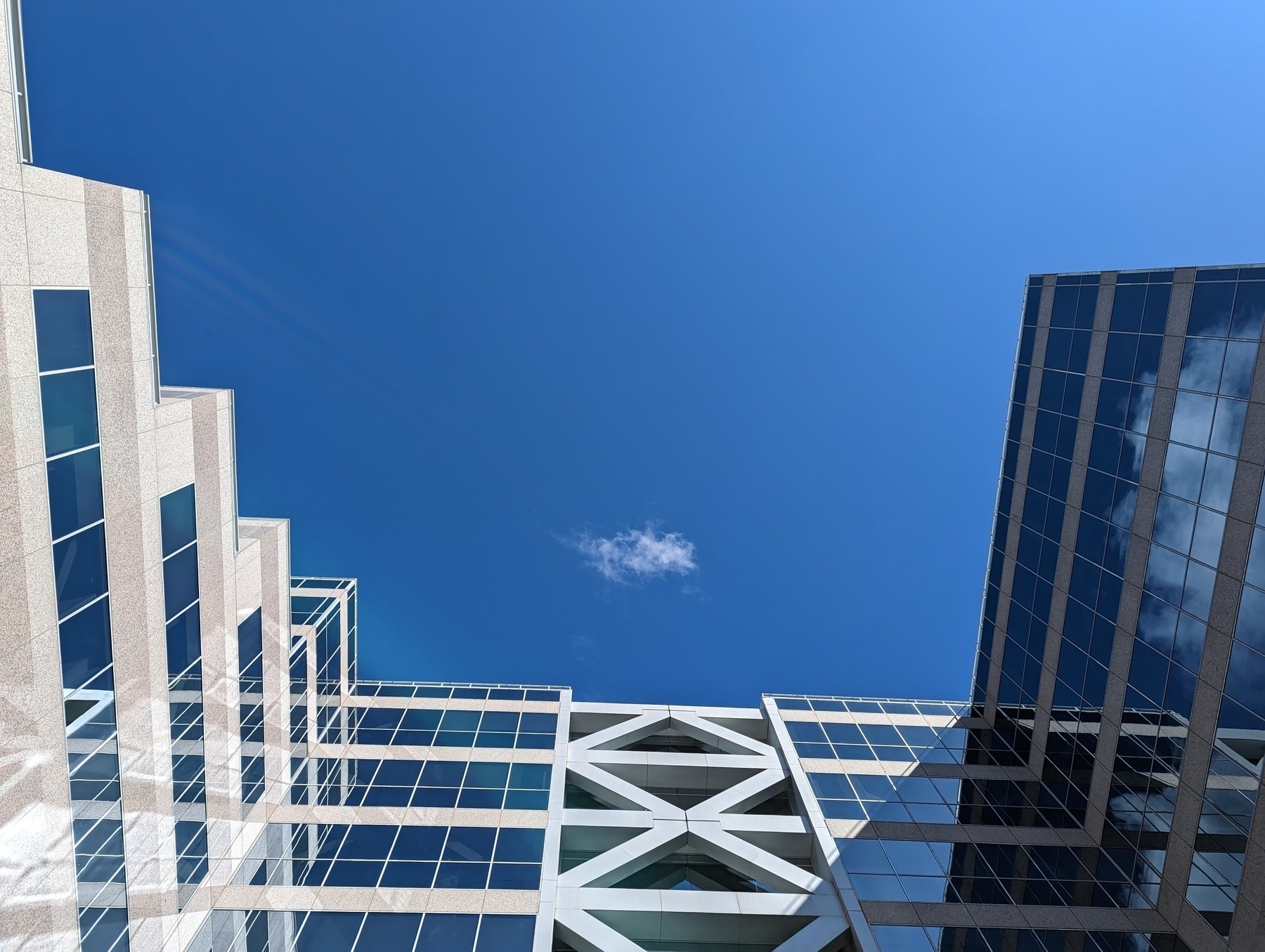 A small white cloud in deep blue sky directly overhead and framed loosely on three sides by shiny glass windows within building walls at the California Plaza office complex Wednesday, March 8, 2023 in the 2100 block of North California Boulevard in Walnut Creek, California.