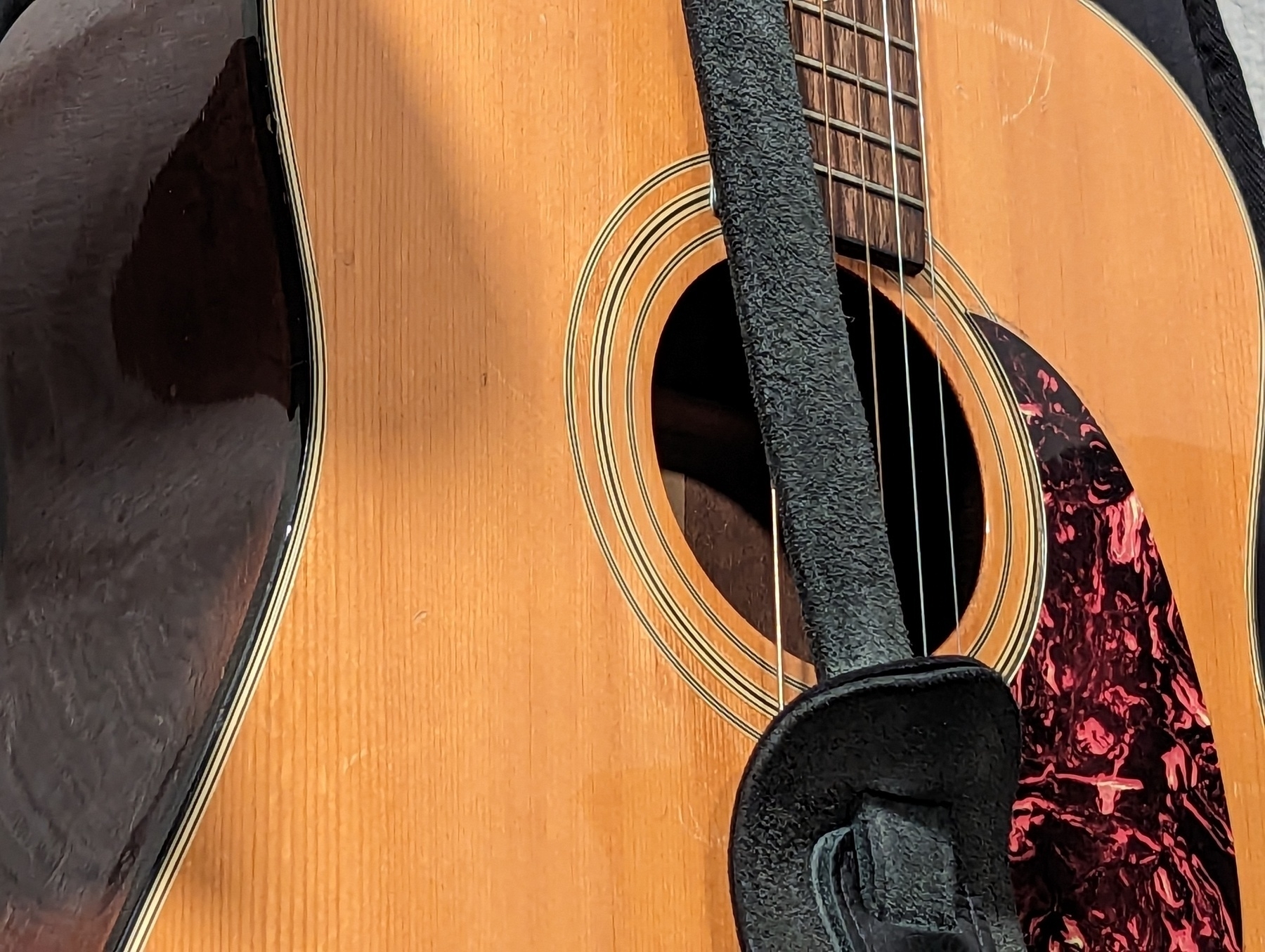 The backside of a black leather guitar strap hangs off the front of my Gibson Epiphone acoustic guitar Saturday, March 25, 2023 in San Pablo, California.