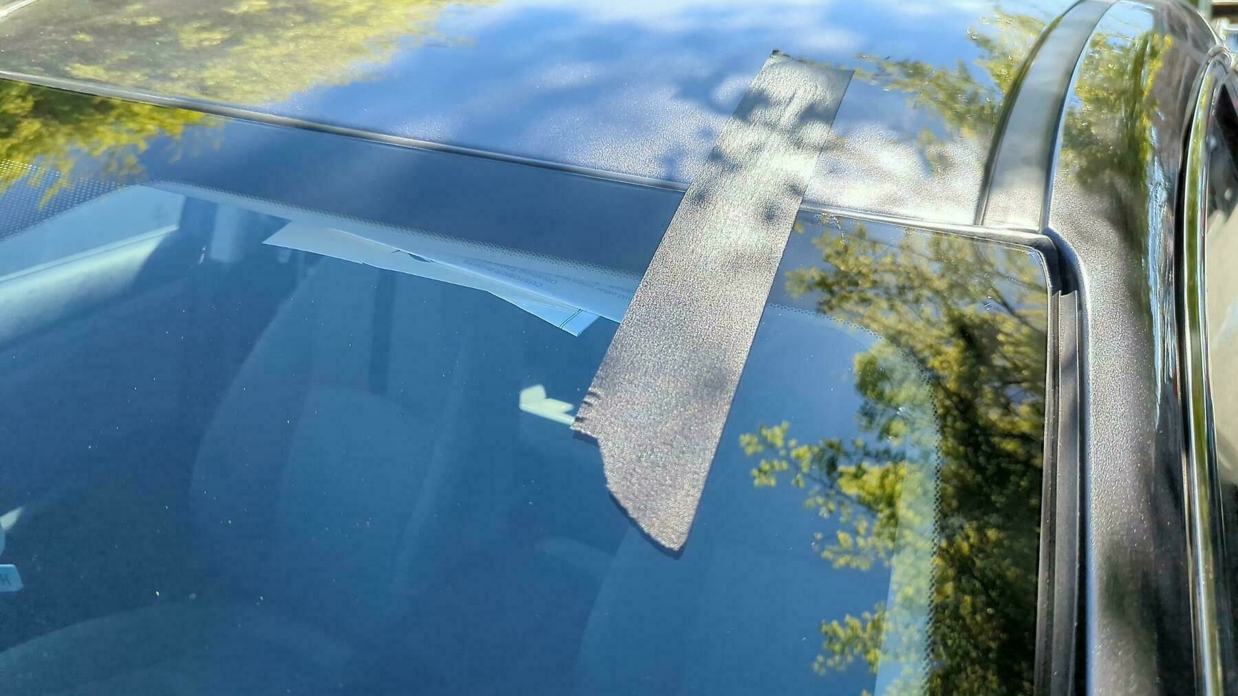 Shadows and sunshine reflect against a foot long piece of gray tape fastened to a newly installed glass car windshield Friday, March 24, 2023 in Oakland, California.