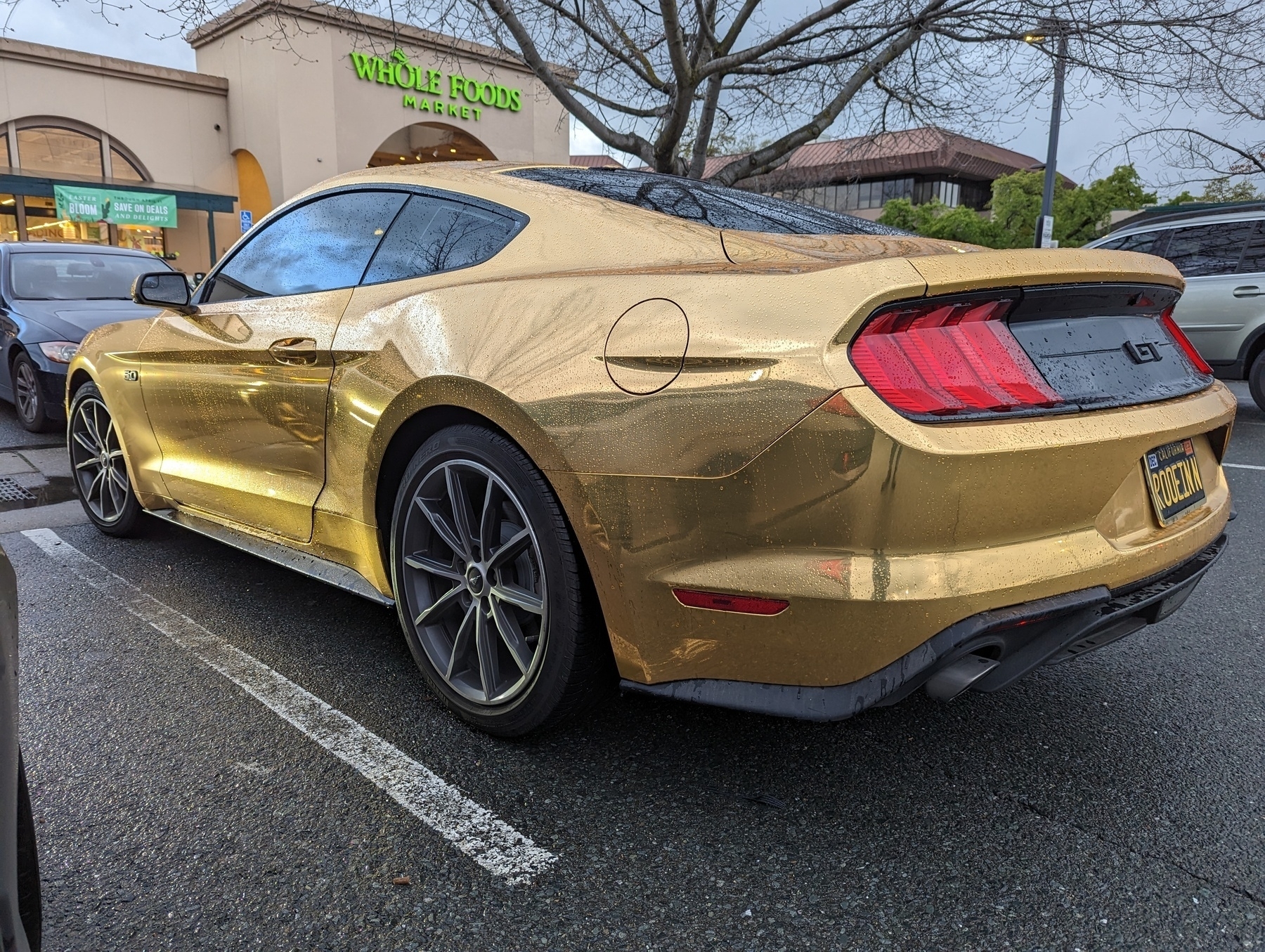 A metallic gold plated Ford Mustang sitting in a parking lot outside a Whole Foods Market grocery store Wednesday, March 29, 2023 in Walnut Creek, California.
