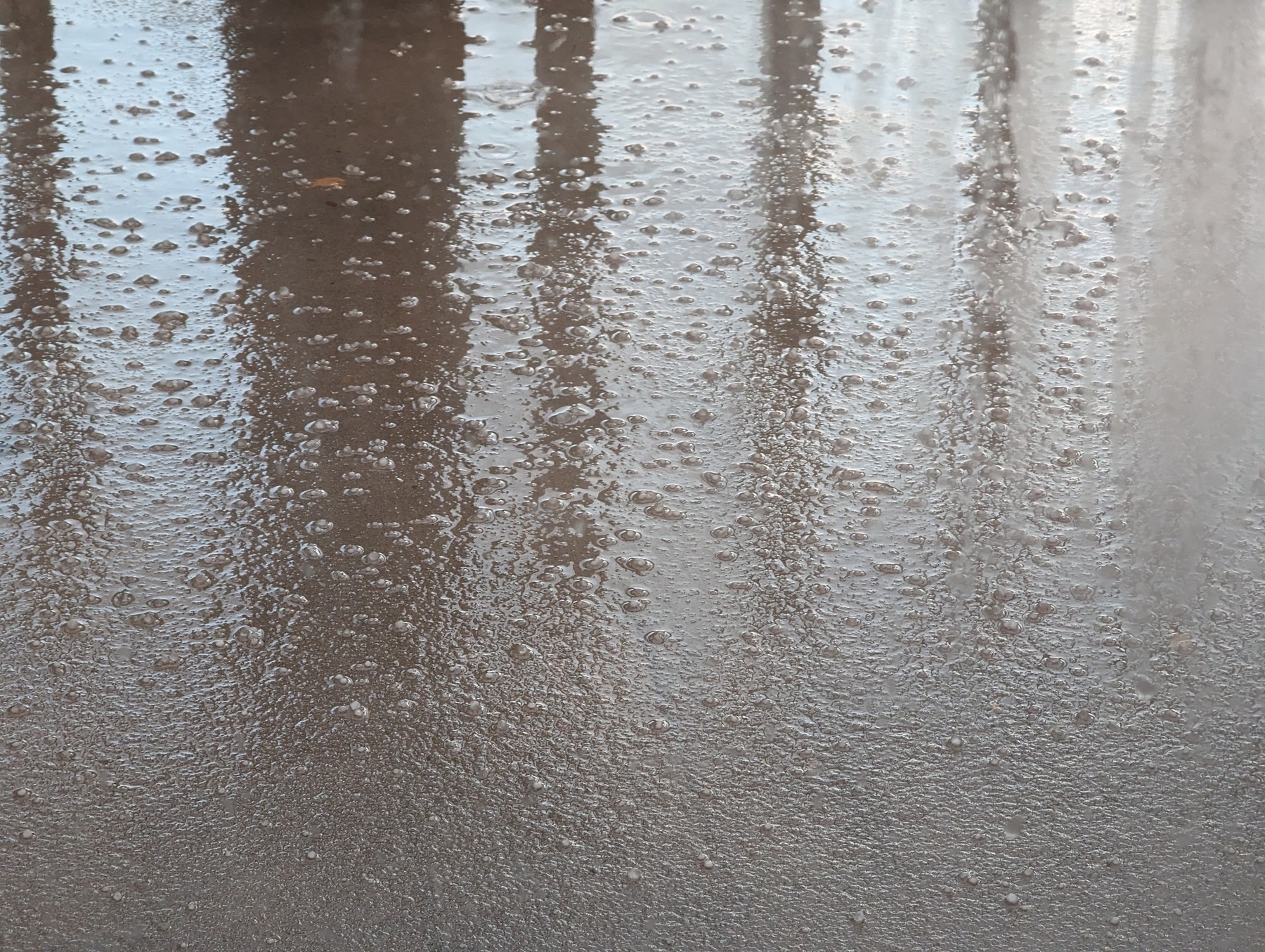 A scattering of hail spread across the patio concrete reflecting nearby wooden railings and wet with fallen rain from one of several storms Monday, March 6, 2023 swinging down from over San Pablo, California.