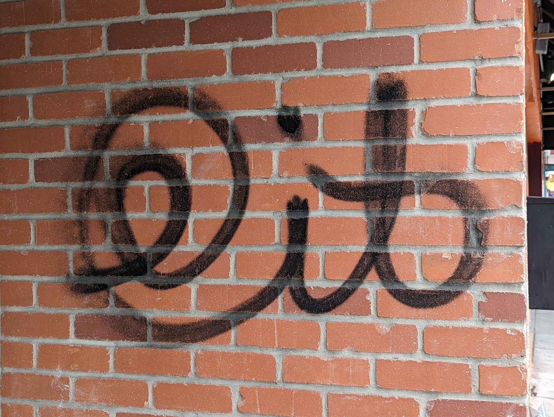 An at symbol and the word "it"  painted in black cursive spray paint on a brick wall on MacArthur Boulevard in Oakland, California's Laurel district Sunday, April 23, 2023.