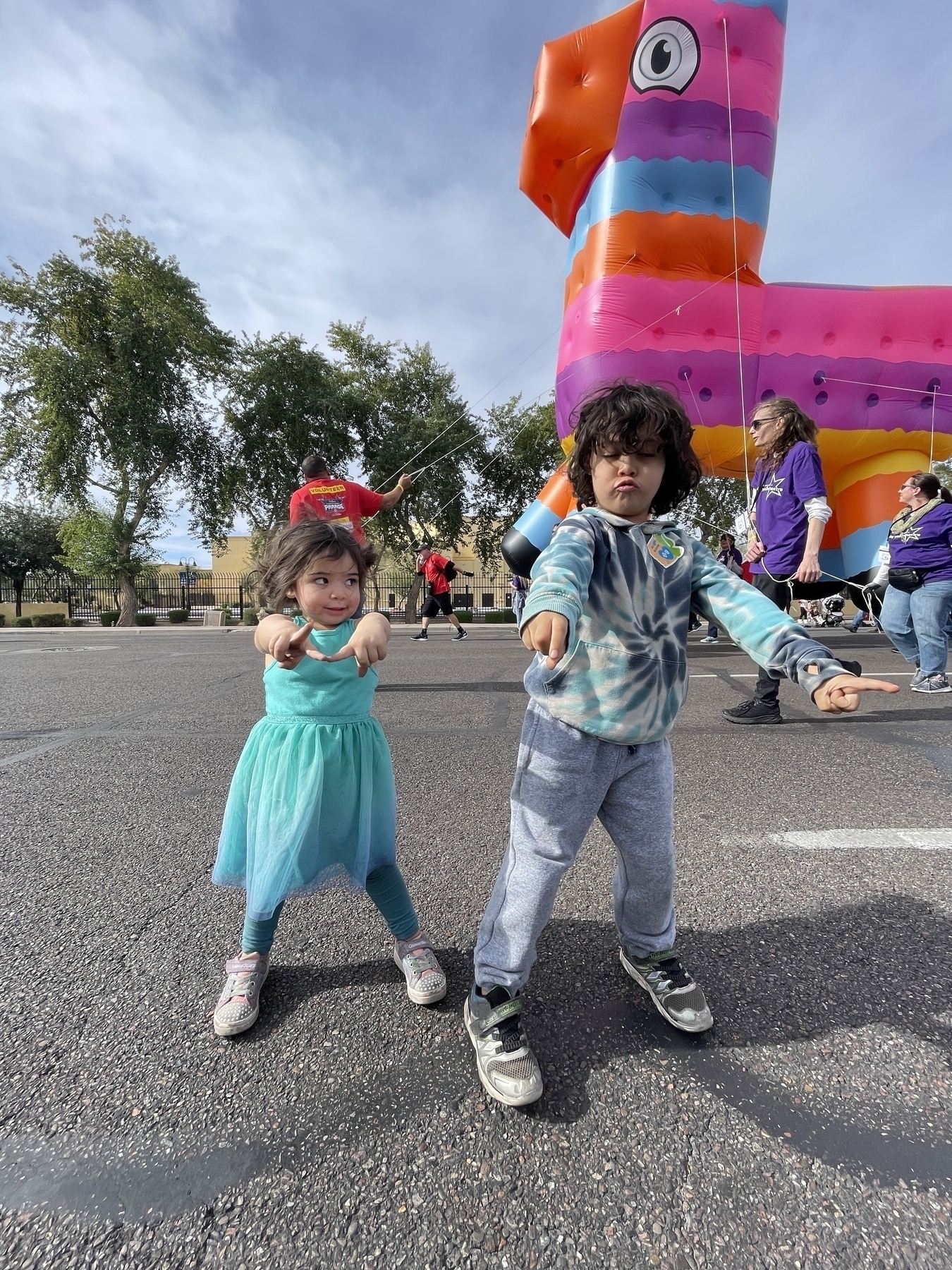 Two young children dancing in front of large piñata parade float