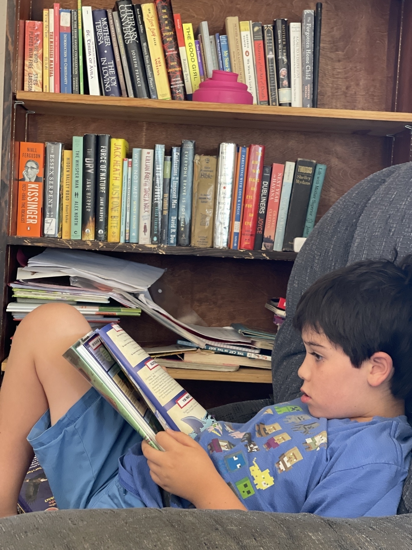 Kid reading a book curled up on chair next to bookcase