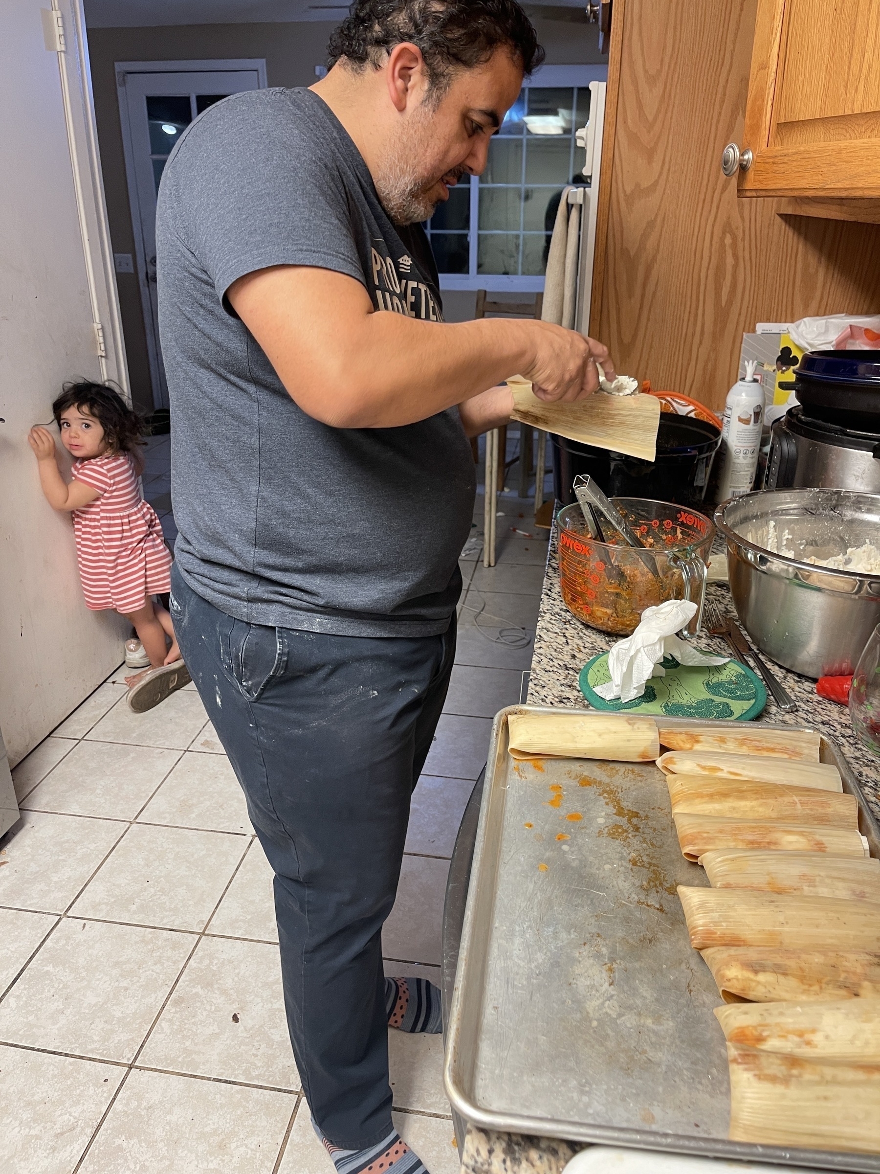 Toddler girl looking at dad while he makes tamales