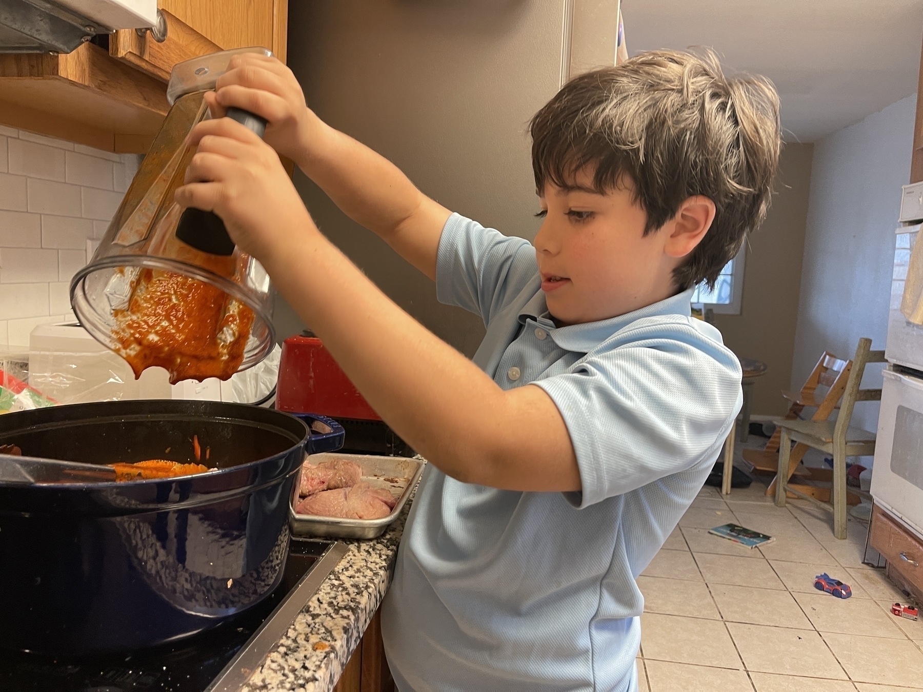 Young boy pouring red sauce into cooking pot
