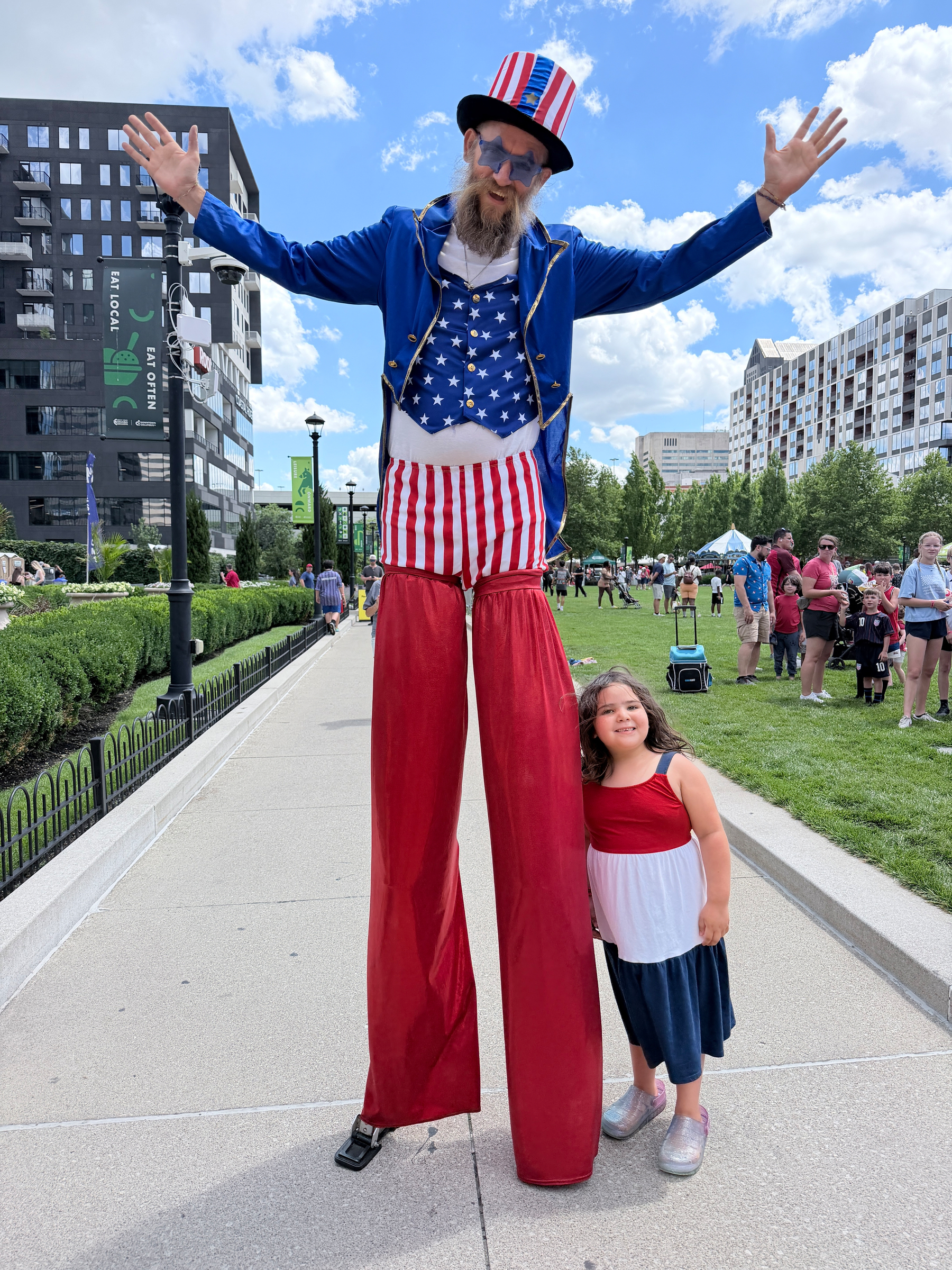Little girl stands next to Uncle Sam on stilts