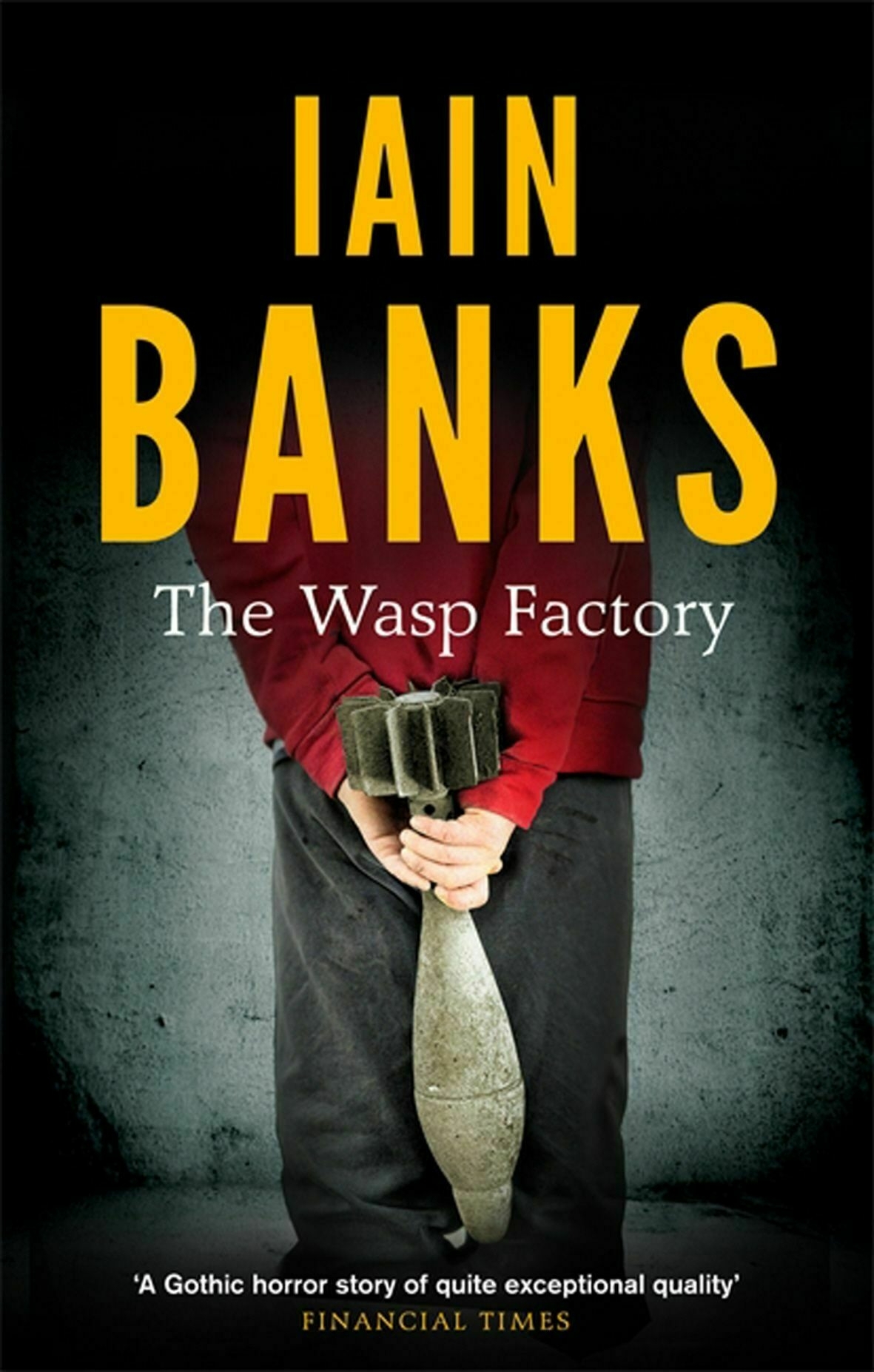Auto-generated description: A person in a red shirt holds a bomb with their hands behind their back on the cover of The Wasp Factory by Iain Banks.
