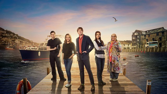 Auto-generated description: A group of five people stands on a dock with a picturesque waterfront and a boat in the background.