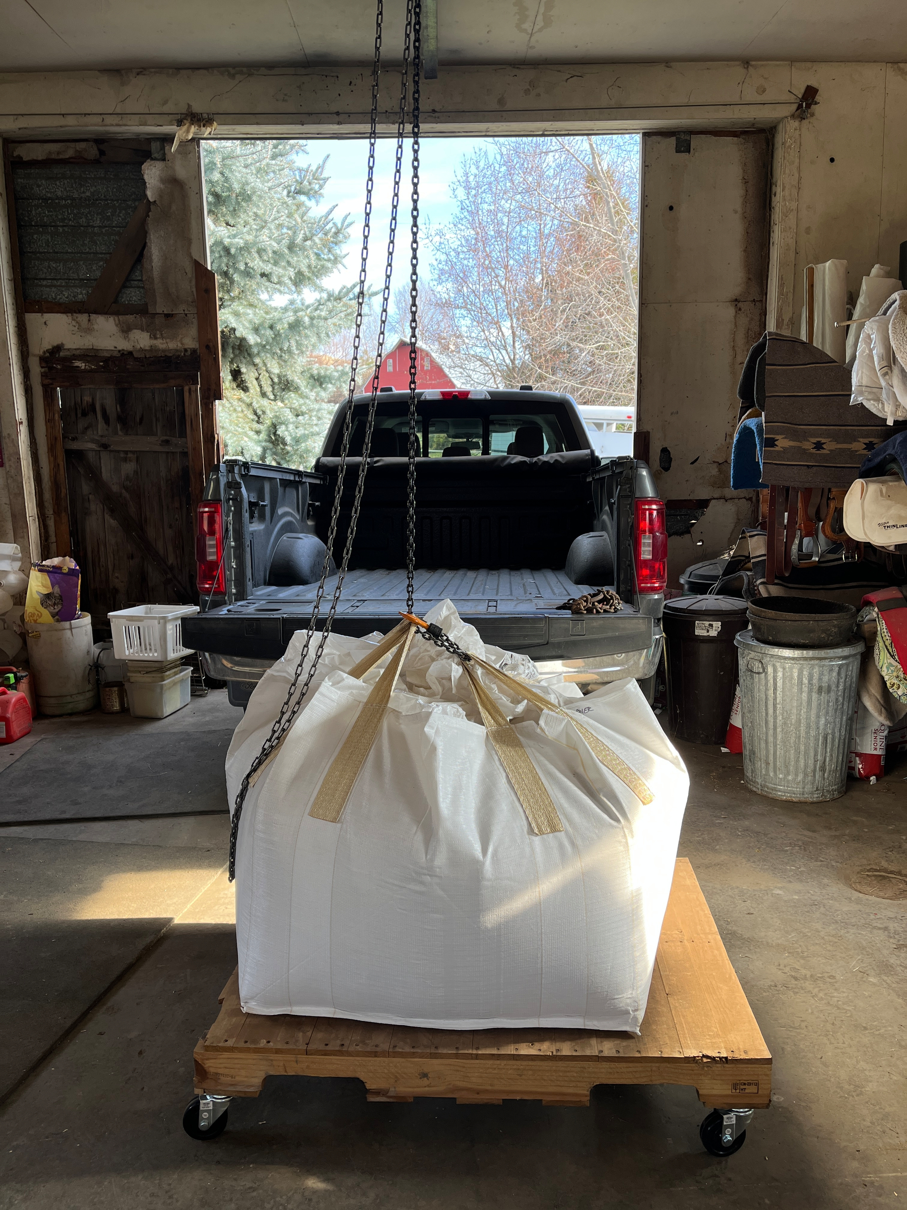 A large white bag suspended by chains is being moved near a pickup truck in an open garage.
