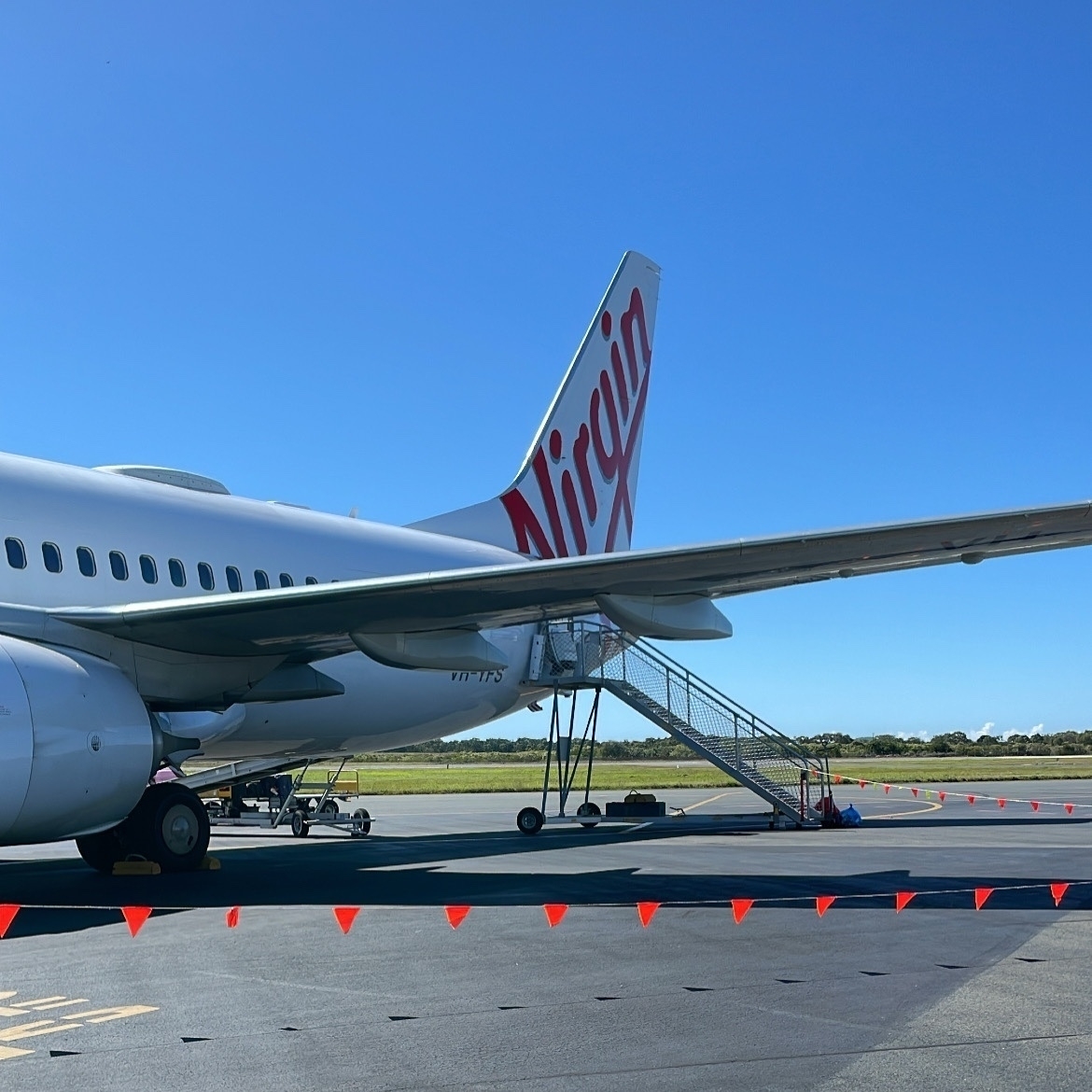 A Virgin Australia plane on the tarmac. 'Virgin' painted in red on the tail. A clear blue sky in the background.