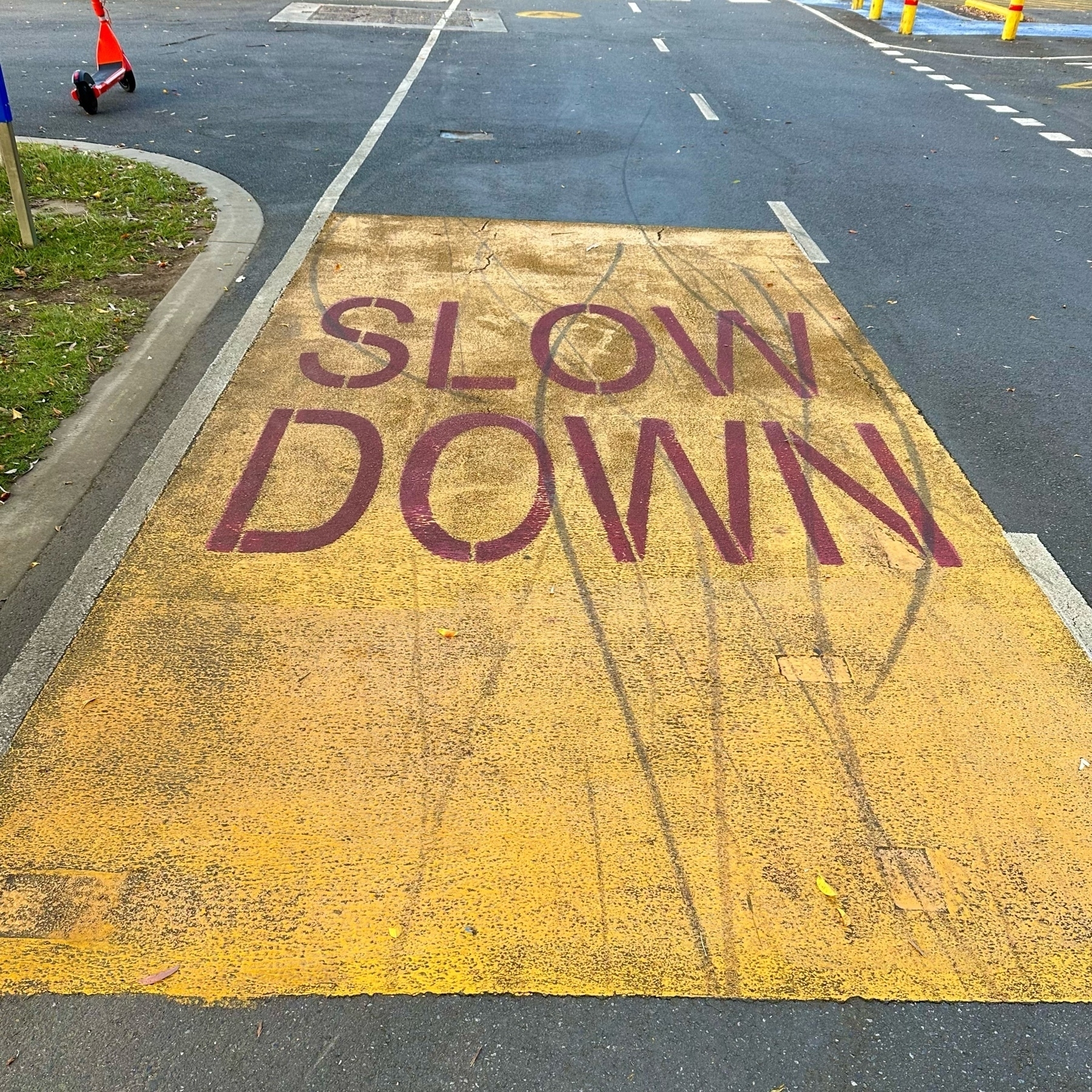 A large yellow rectangular box painted longways on the road. "Slow down" is painted in large red capital letters in the top half.