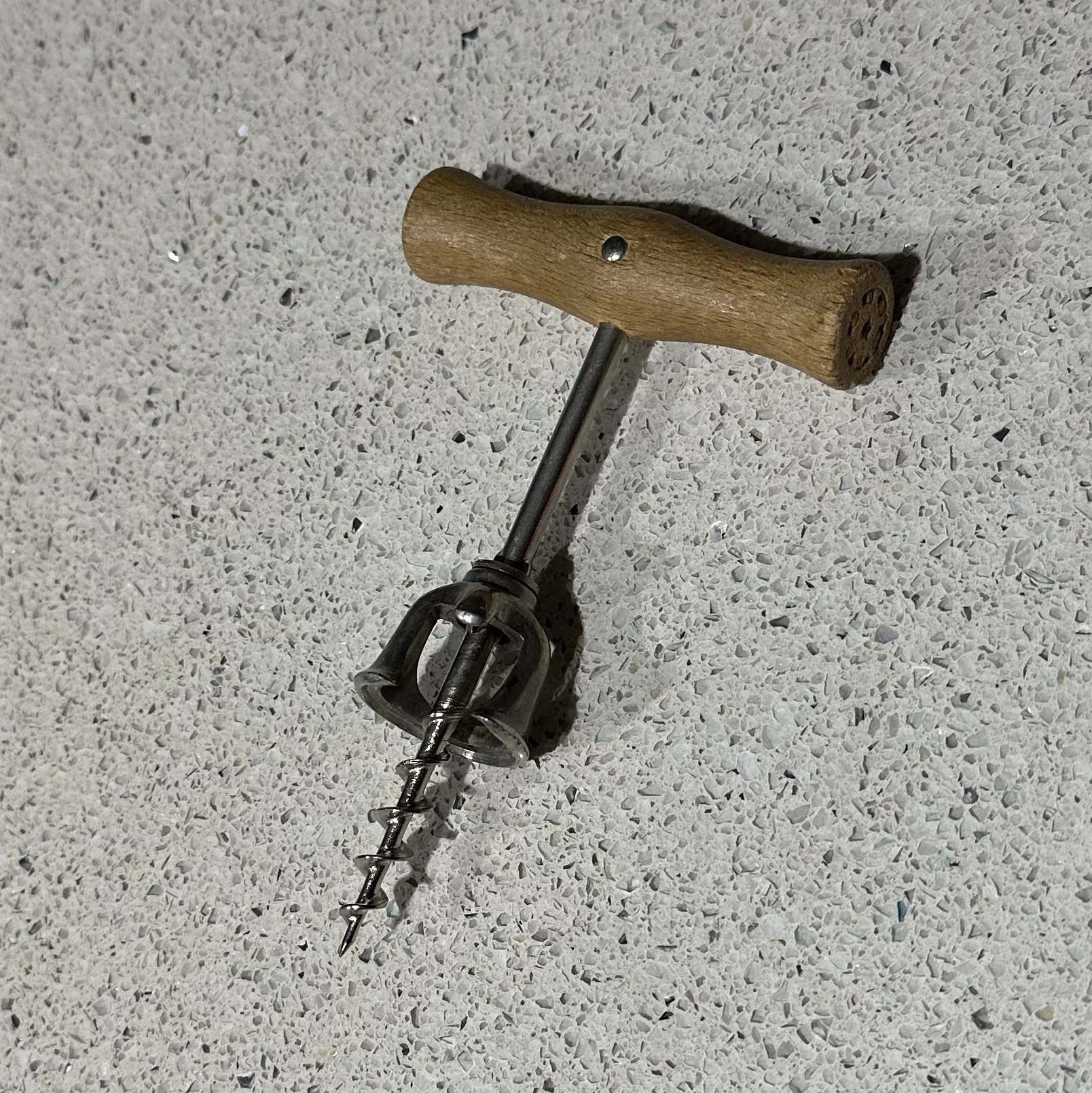 A metal corkscrew with a simple wooden handle and a bell shape stopper about two thirds of the way along to pull the cork up into.