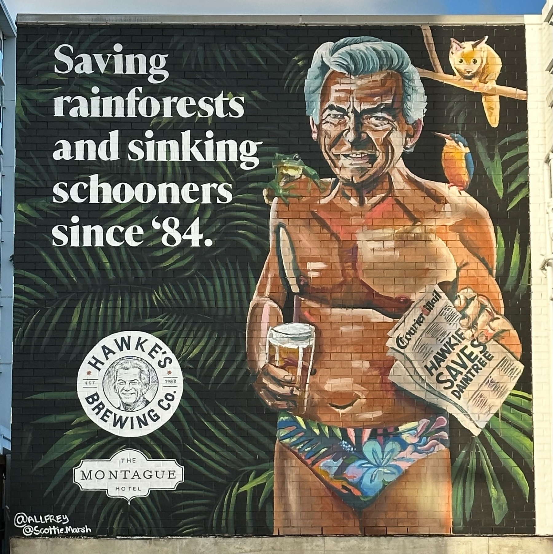 Advertising for Hawke’s Brewing painted on a brick wall. Top left says “Saving rainforests and sinking schooners since ‘84.” Bottom left has the company logo and “Montague Hotel”. The right half has former Australian prime minister Bob Hawke in speedos, holding a beer and newspaper a bird and frog on either shoulder and a possum on a branch behind him.