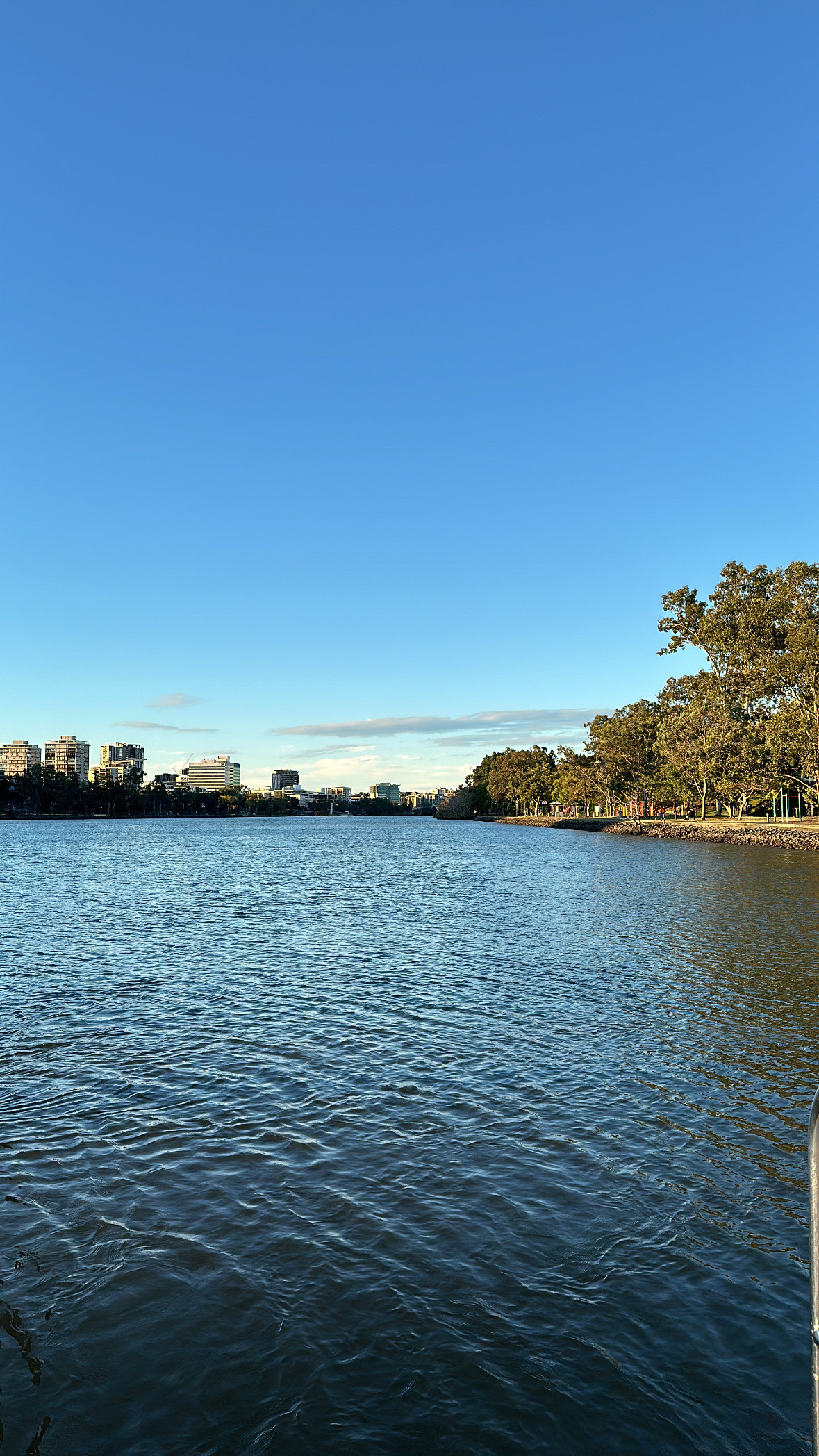 Looking along the Brisbane River. The lower half of the photo is the blue of the river. The curve of the river creates a thin band of land across the middle with the upper half a clear blue sky.