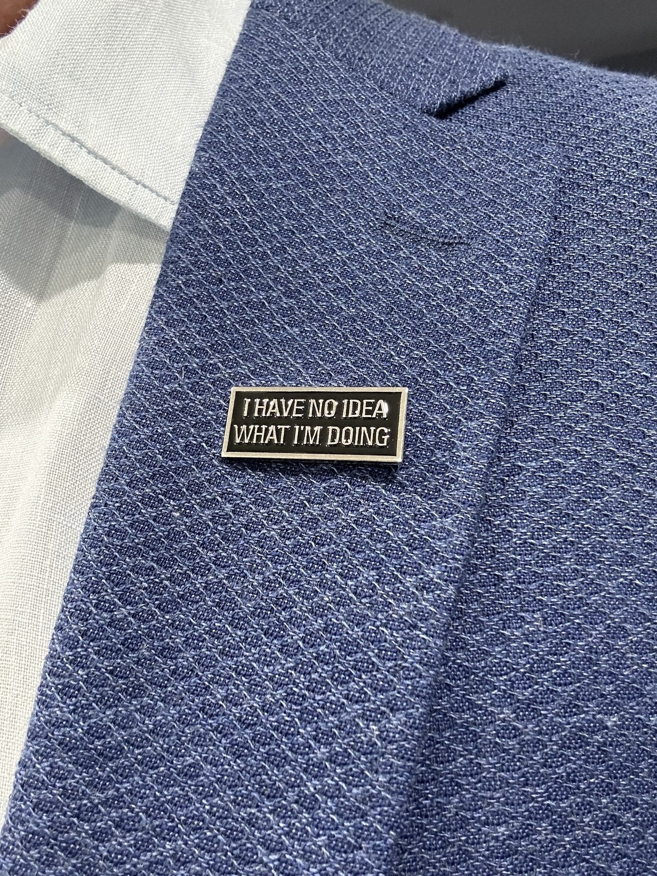 A rectangular silver badge on a blue jacket. The badge says “I have no idea what I’m doing”
