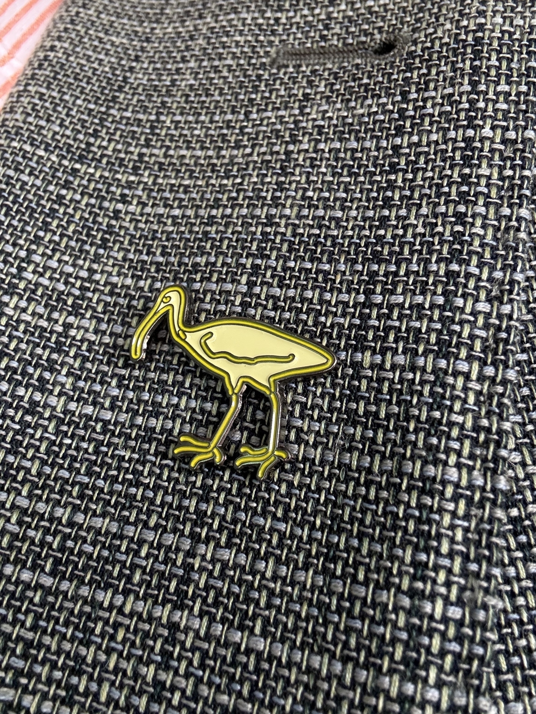 An enamel badge shaped like the Ibis bird pinned to a jacket.