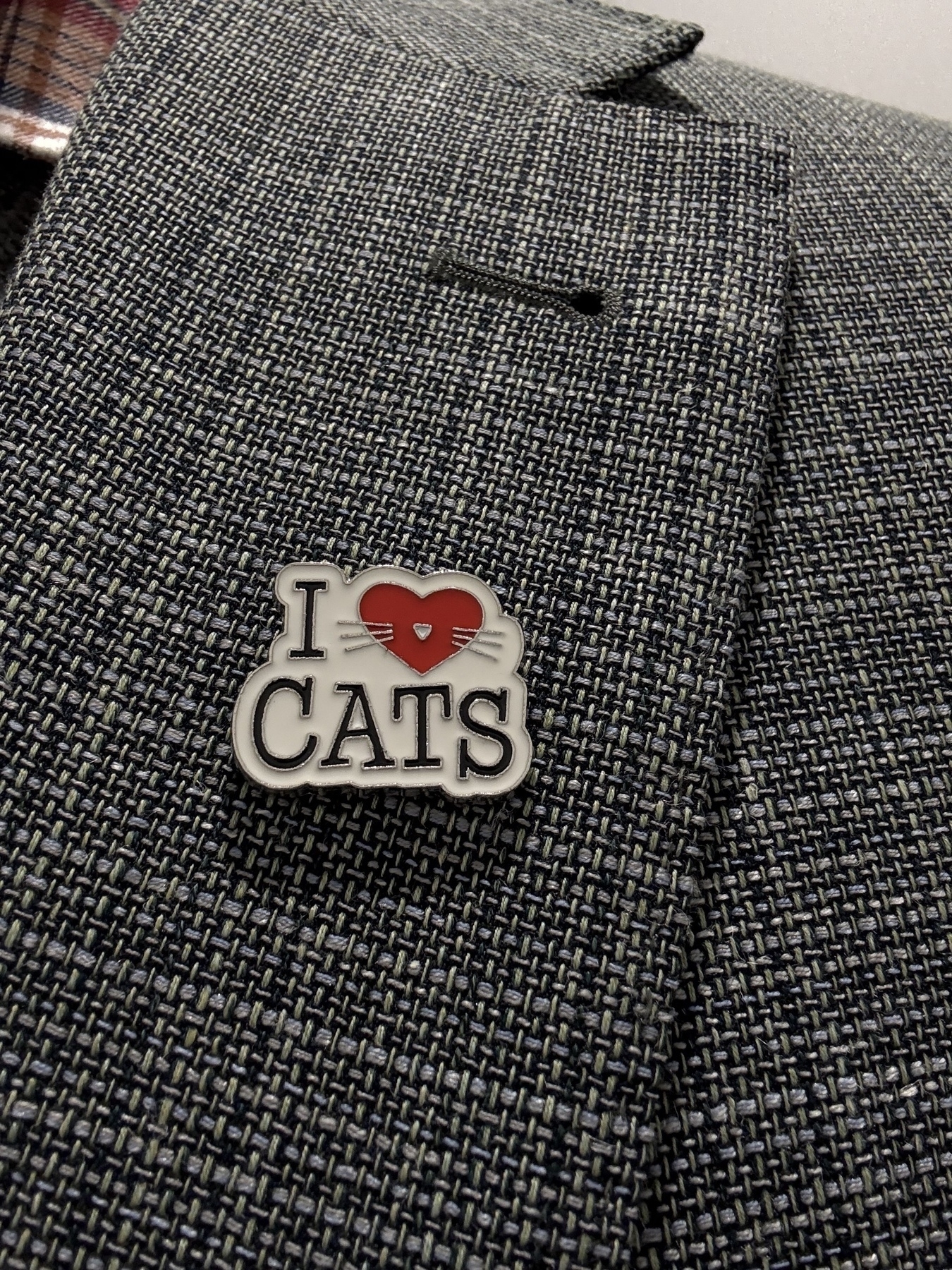An enamel badge pinned to a suit jacket. The badge has a white background and says - I (red heart emoji with whiskers) cats