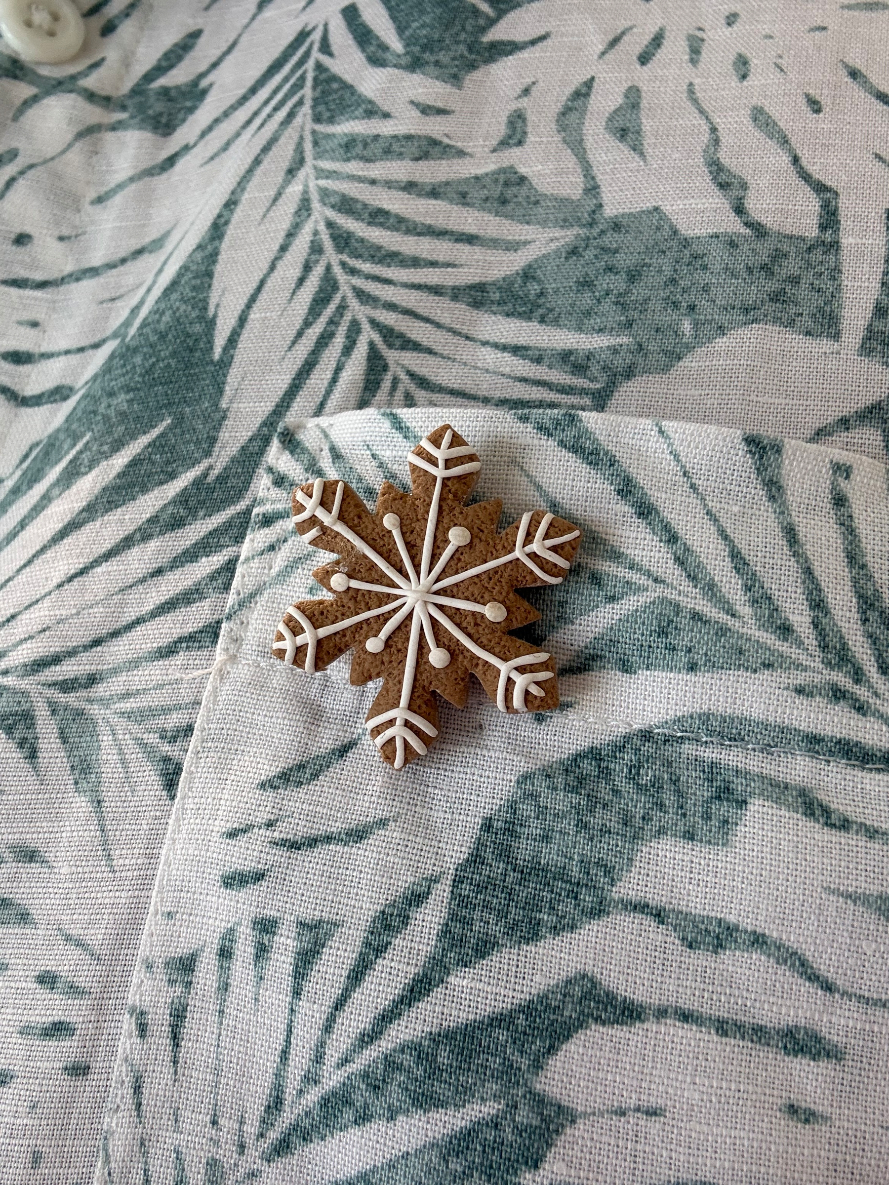 A badge pinned on a green and white shirt. The badge is a six pointed snowflake, gingerbread brown background and white lines to pop the snowflake shape out.