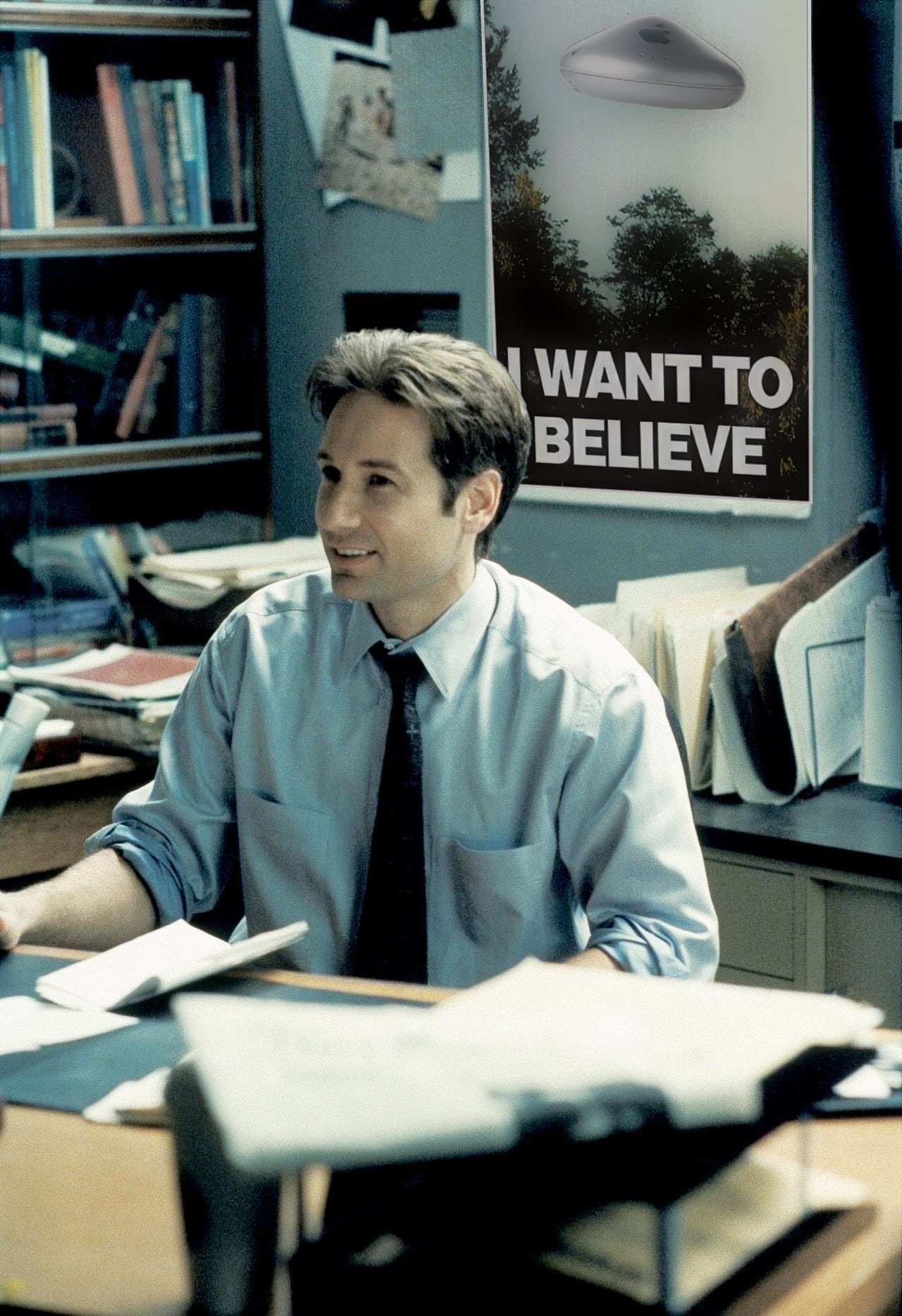 Fox Mulder in the cluttered X-Files basement office with the I Want to Believe poster hung up behind him.