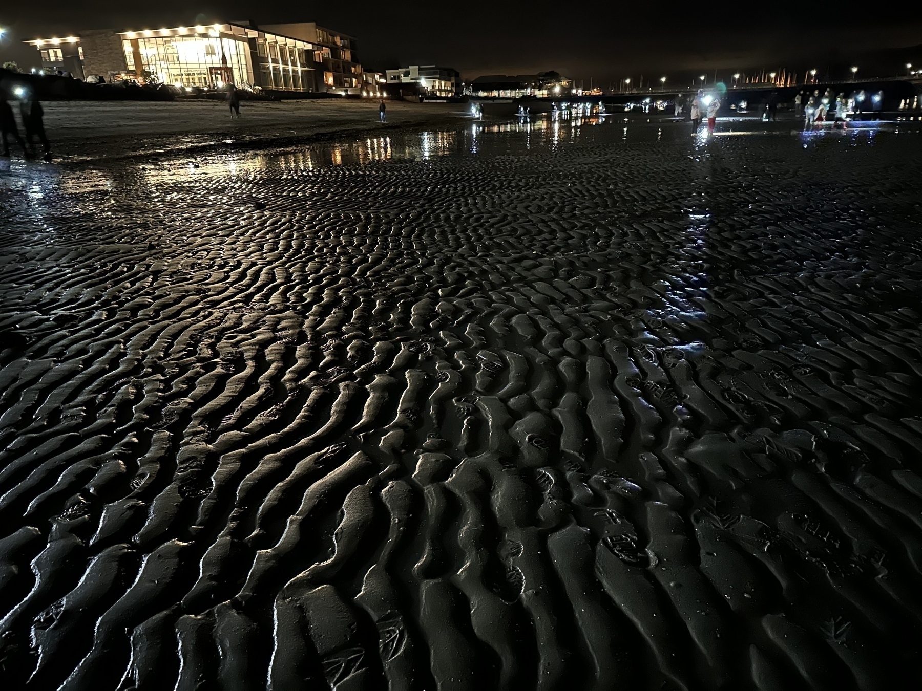 Photo at night of Edmonds Washington beach showing reflected light on wet sand.