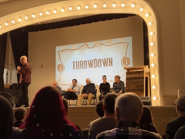 Photo from audience of stage with 4 people sitting and MC standing