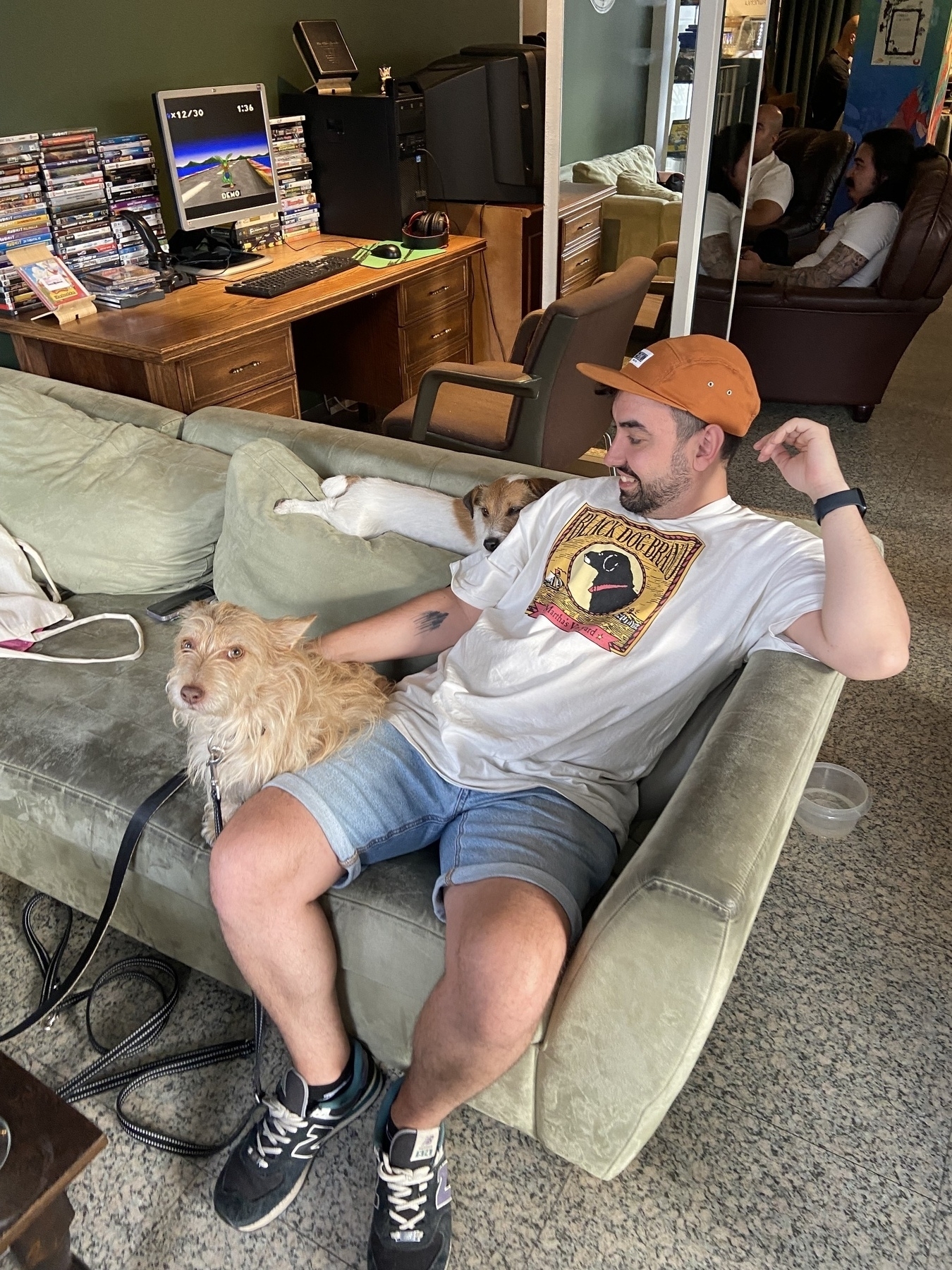 Person in a white t-shirt sitting on a couch with two small dogs at a game bar.
