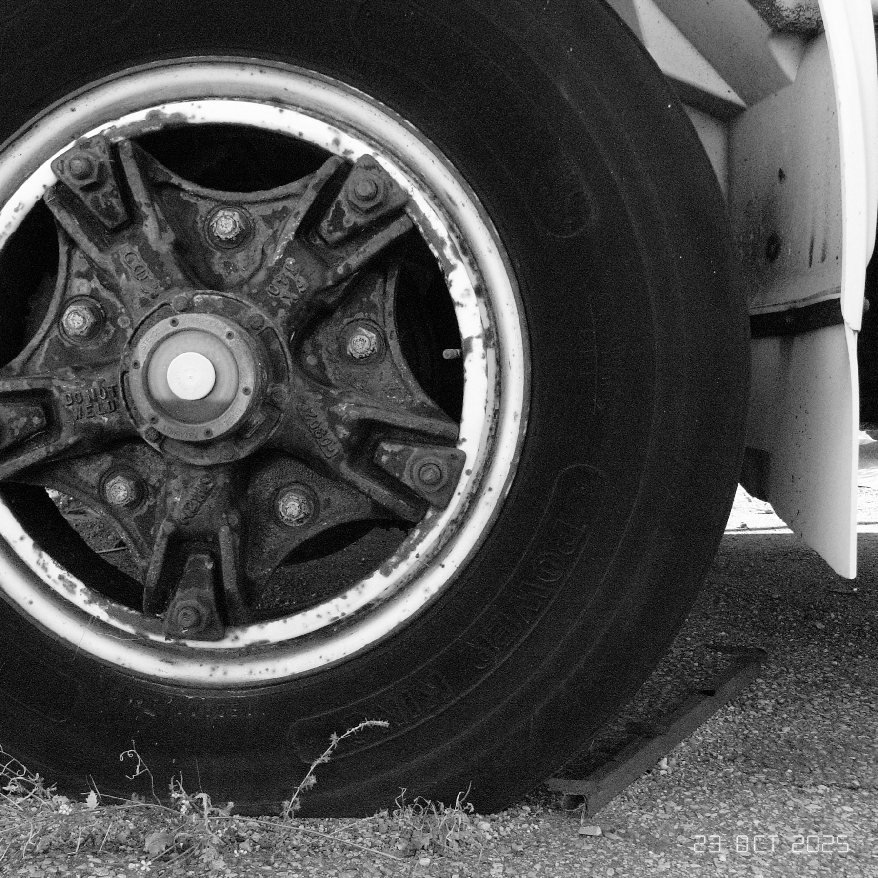 A black and white close-up of a large vehicle wheel with a detailed view of the tire and hubcap.