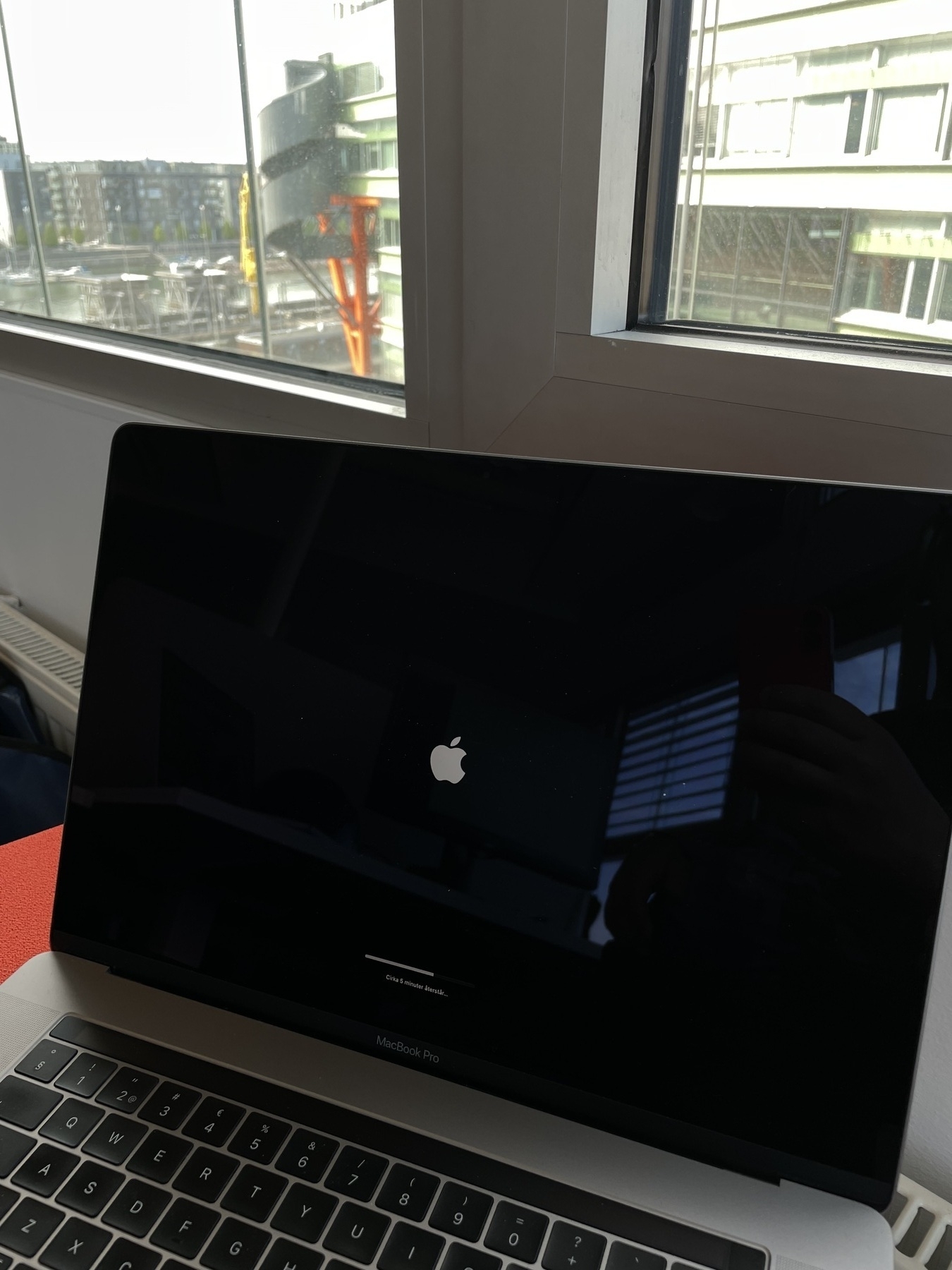 A MacBook Pro showing an Apple logo system update screen with a progress bar and 5 minutes ETA