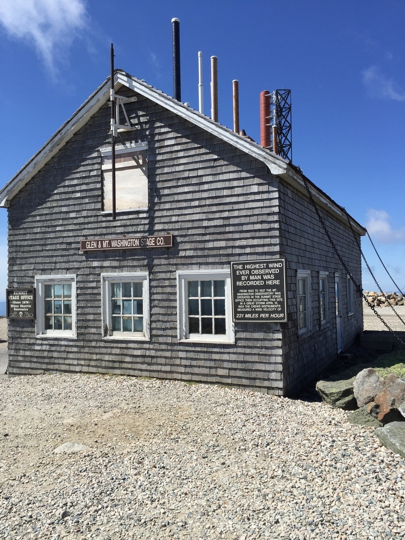 Wooden building on summit that has chains from its roof to the ground and features a sign describing the record setting 231mph winds that were recorded here.