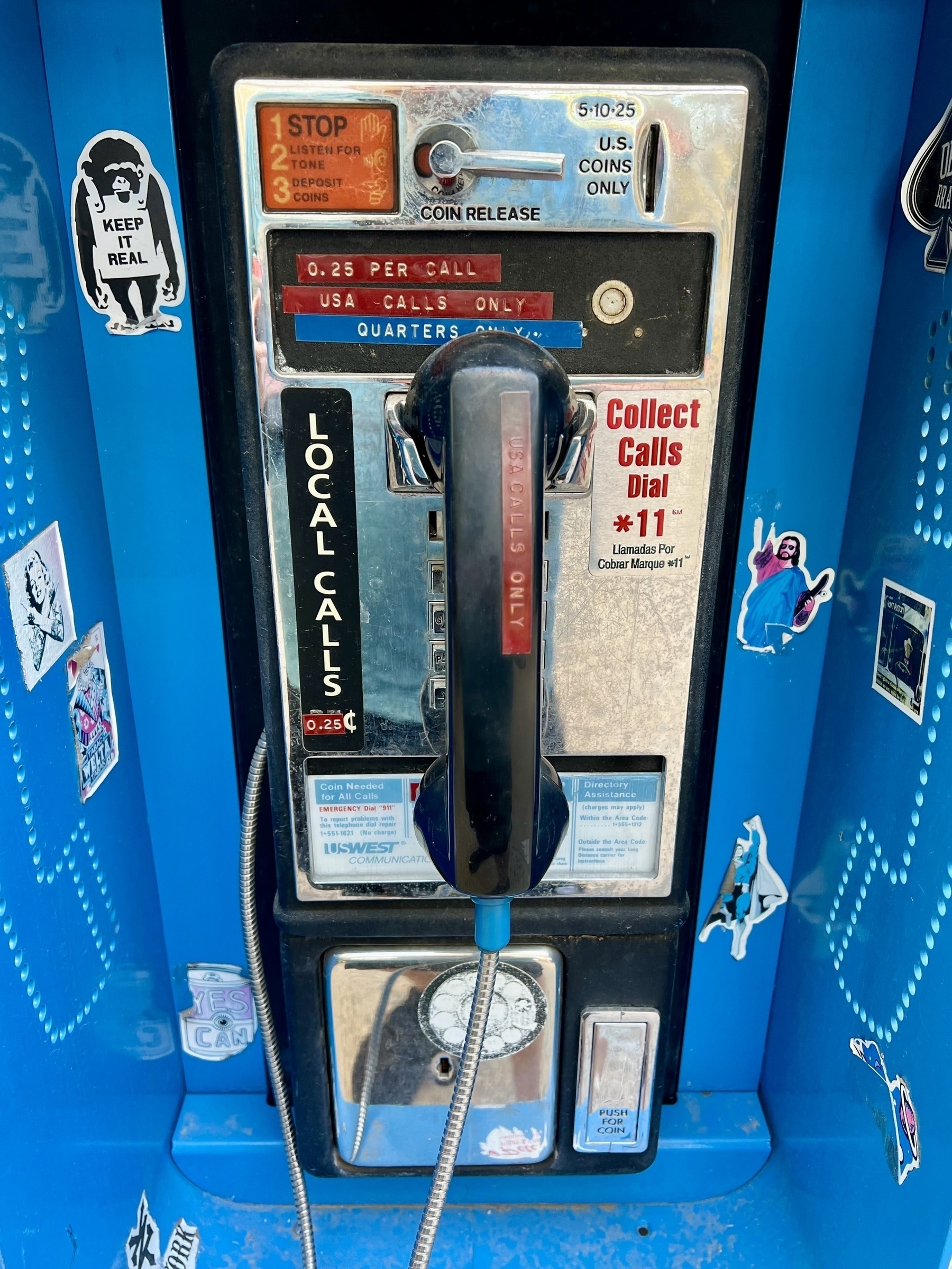 A vintage payphone is adorned with various colorful stickers.