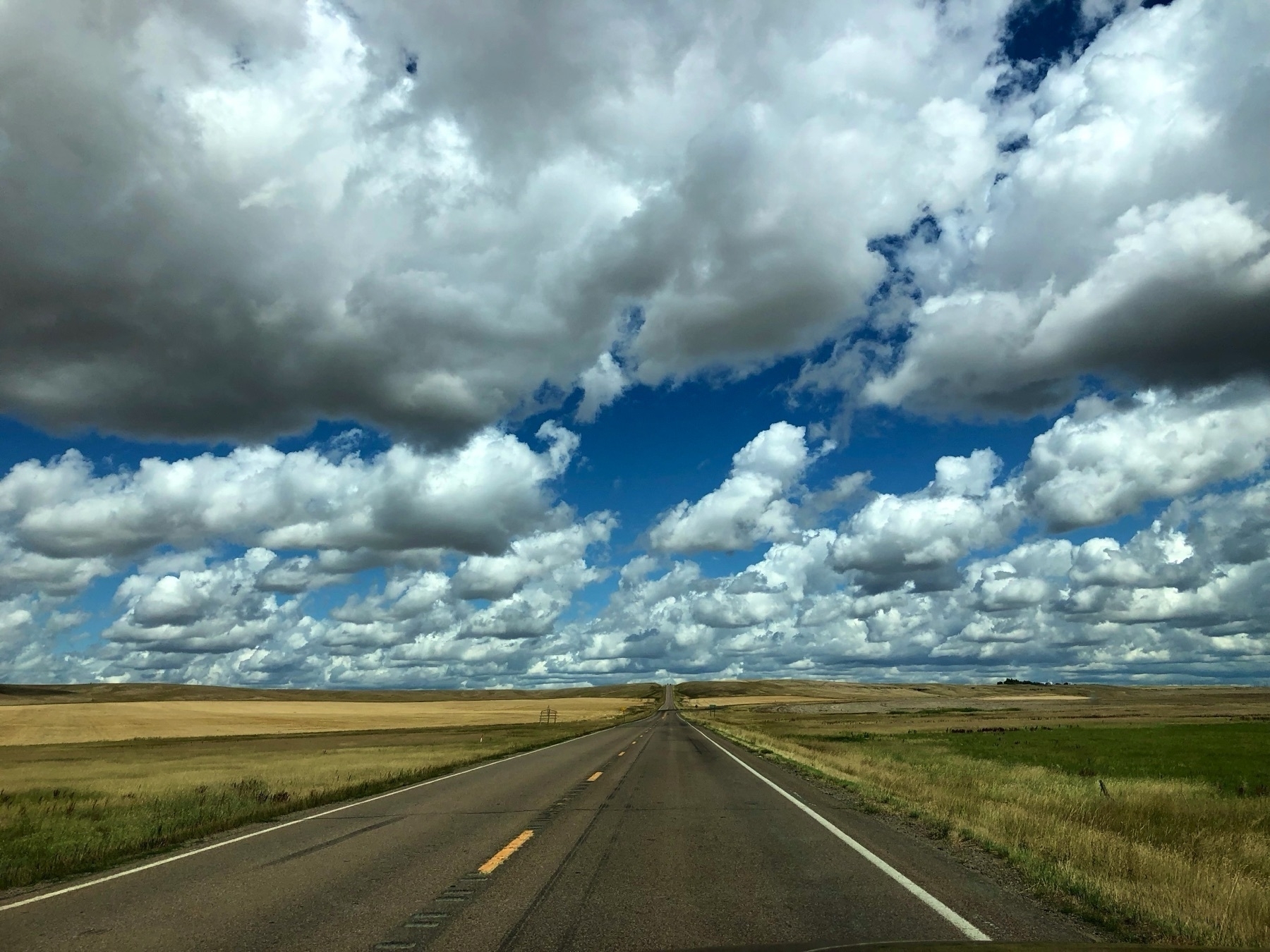 Some kickass clouds dominate trhe scene, with a lonely two lane highway and some beige fields in the foreground.