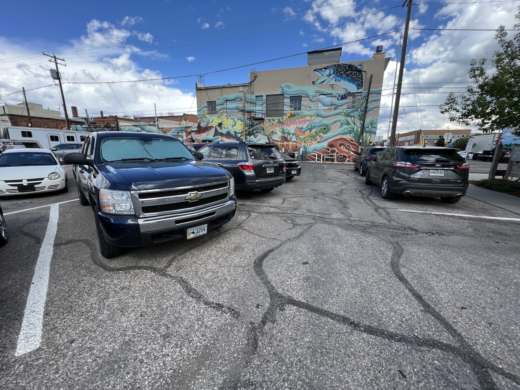 Chevy truck parked in a parking lot with other vehicles behind a building painted with large colorful mural.