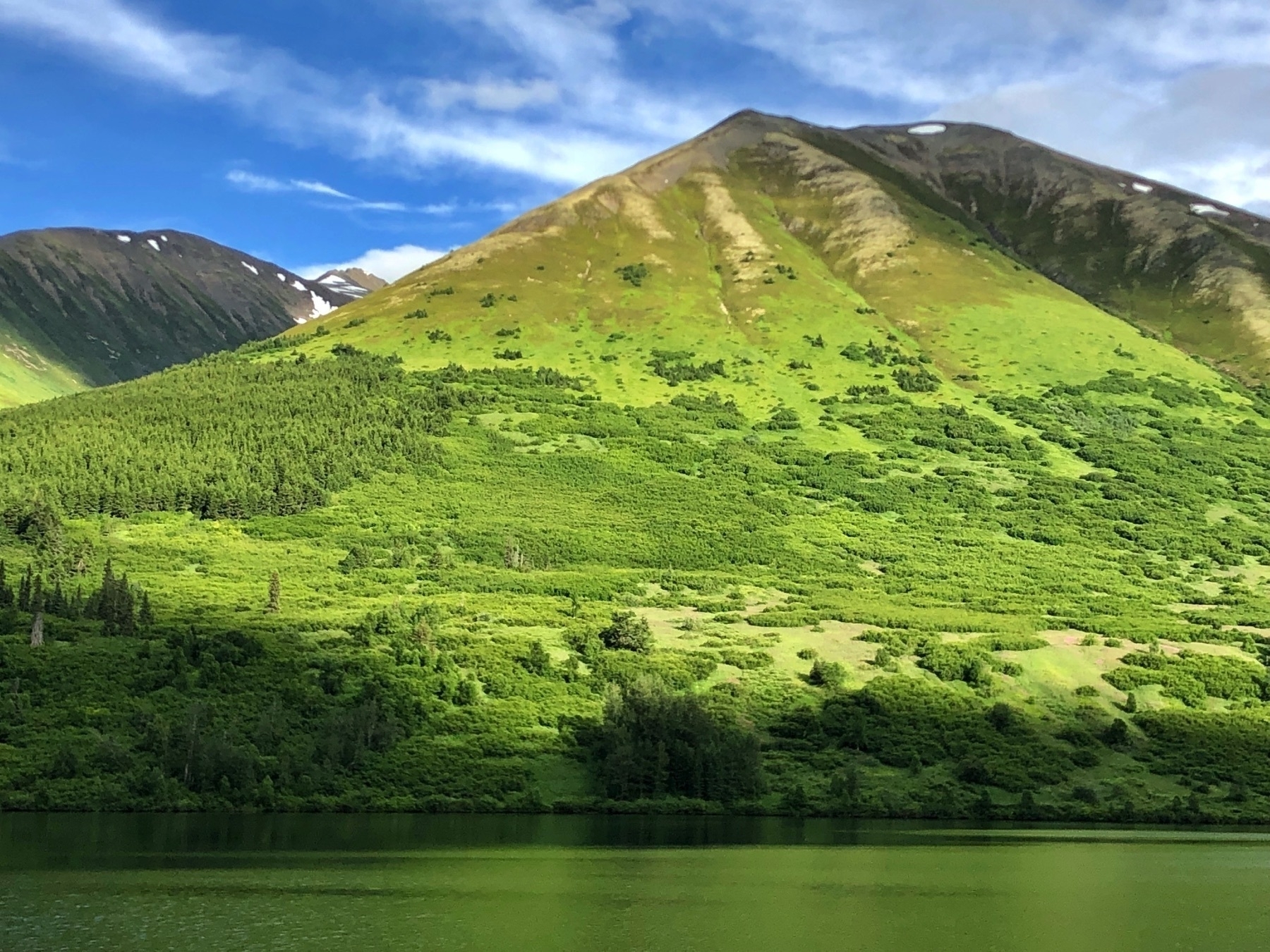 Mountain covered with green vegetation and a sliver of water in the extreme foreground