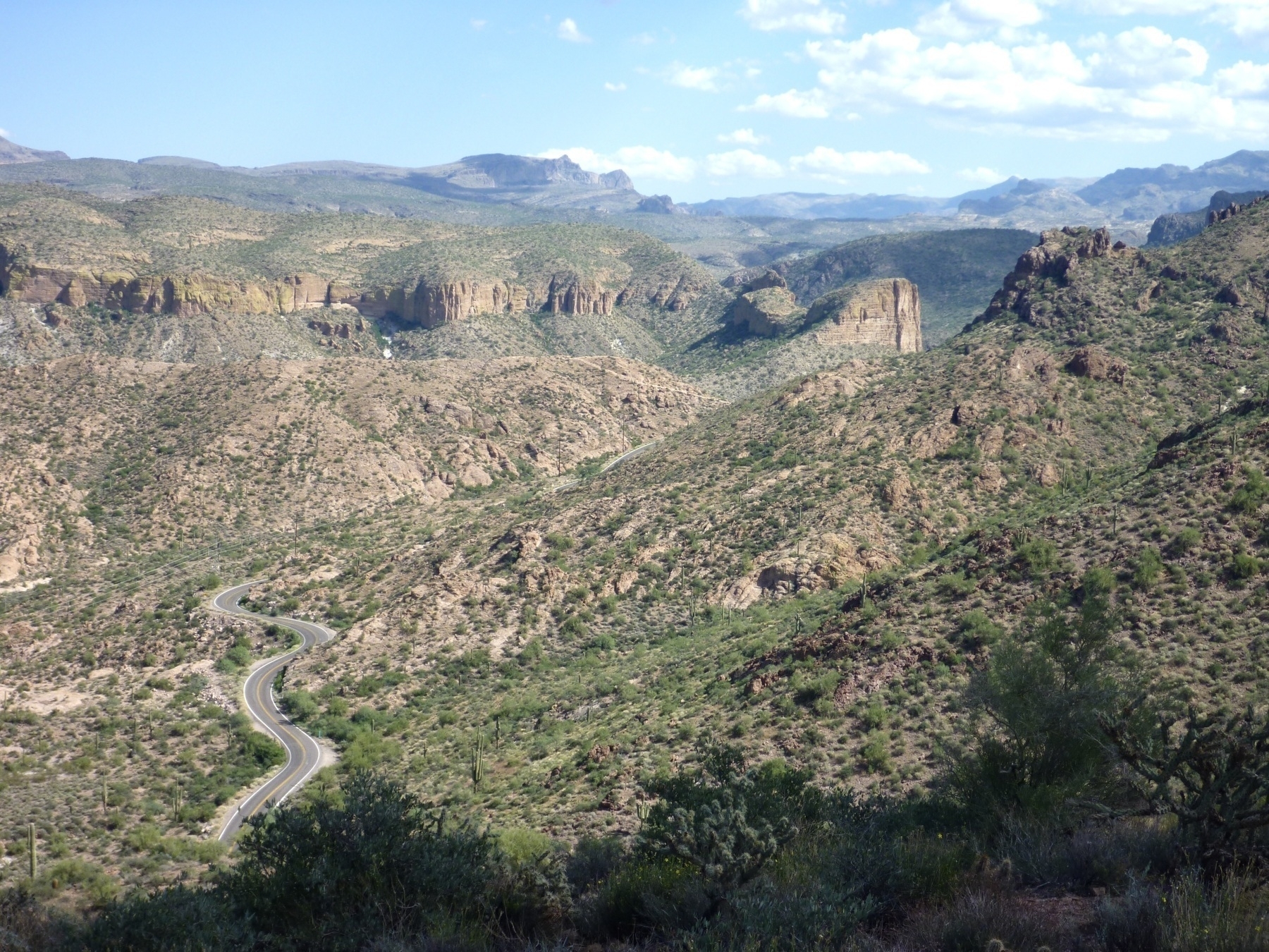 Two lane highway winds into a deserty mountainous wilderness