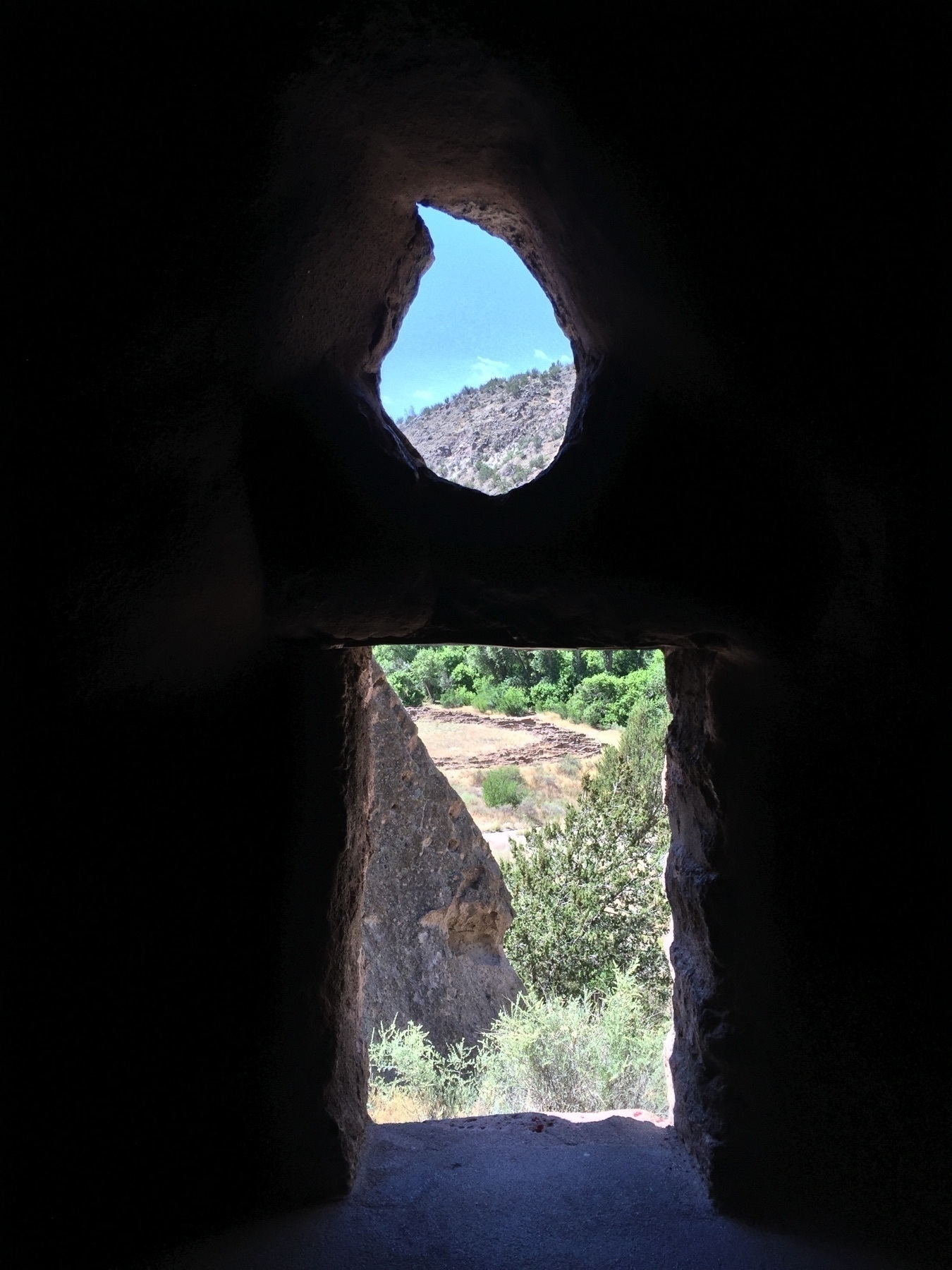 Looking out from a ruin at Bandalier National Monument through a doorway and “window” that resemble a candle or a styled letter “i”