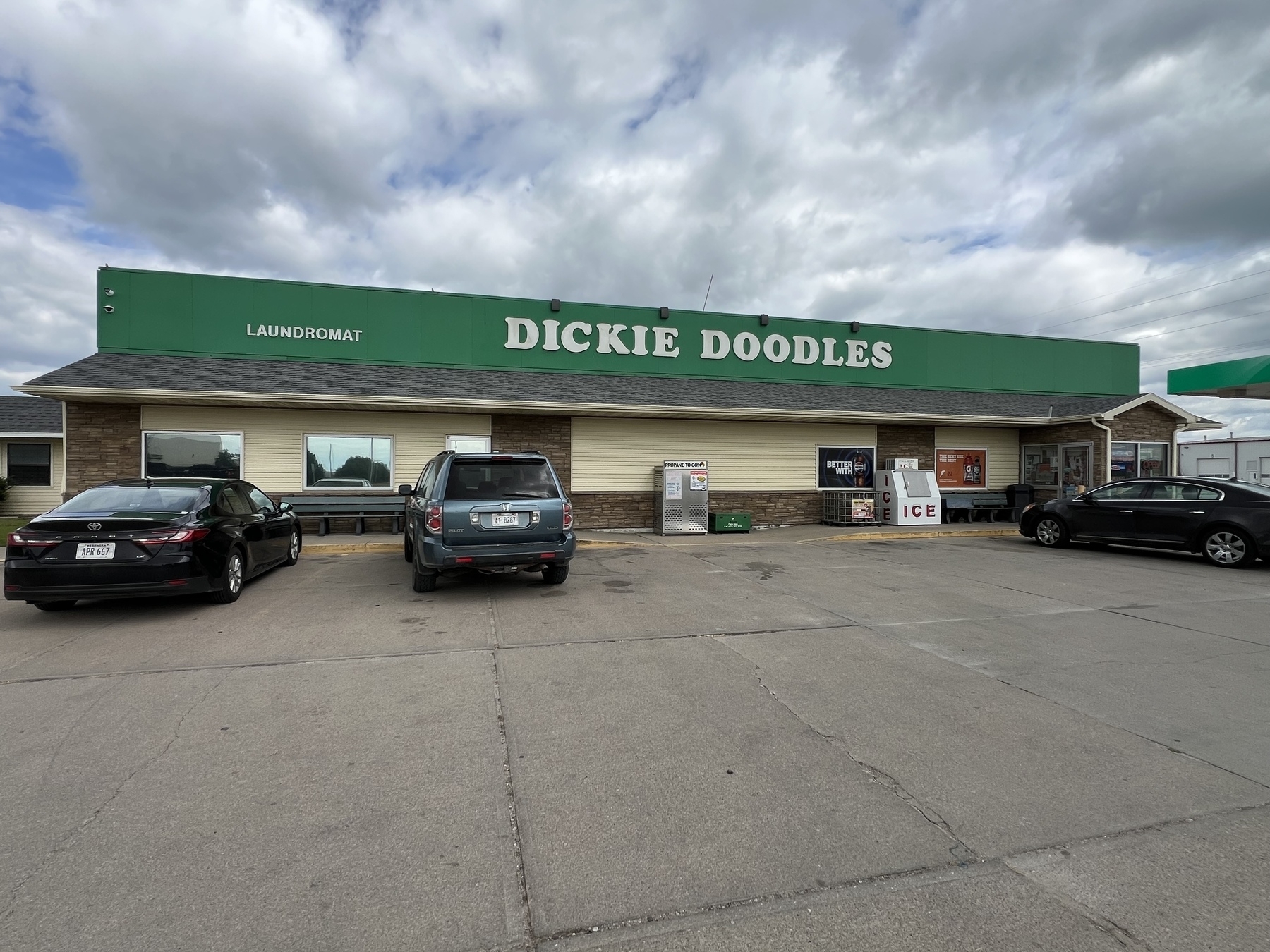 A convenience store named "Dickie Doodles" and laundromat is situated in a parking lot with several cars parked in front.