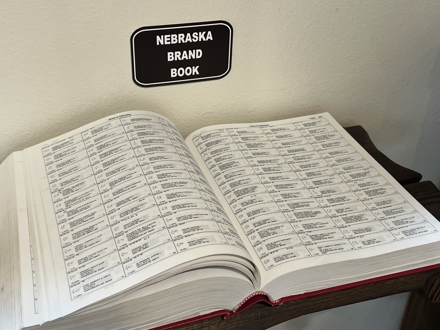 An open book labeled "Nebraska Brand Book" is displayed on a wooden stand, showing pages of text organized in a table format.