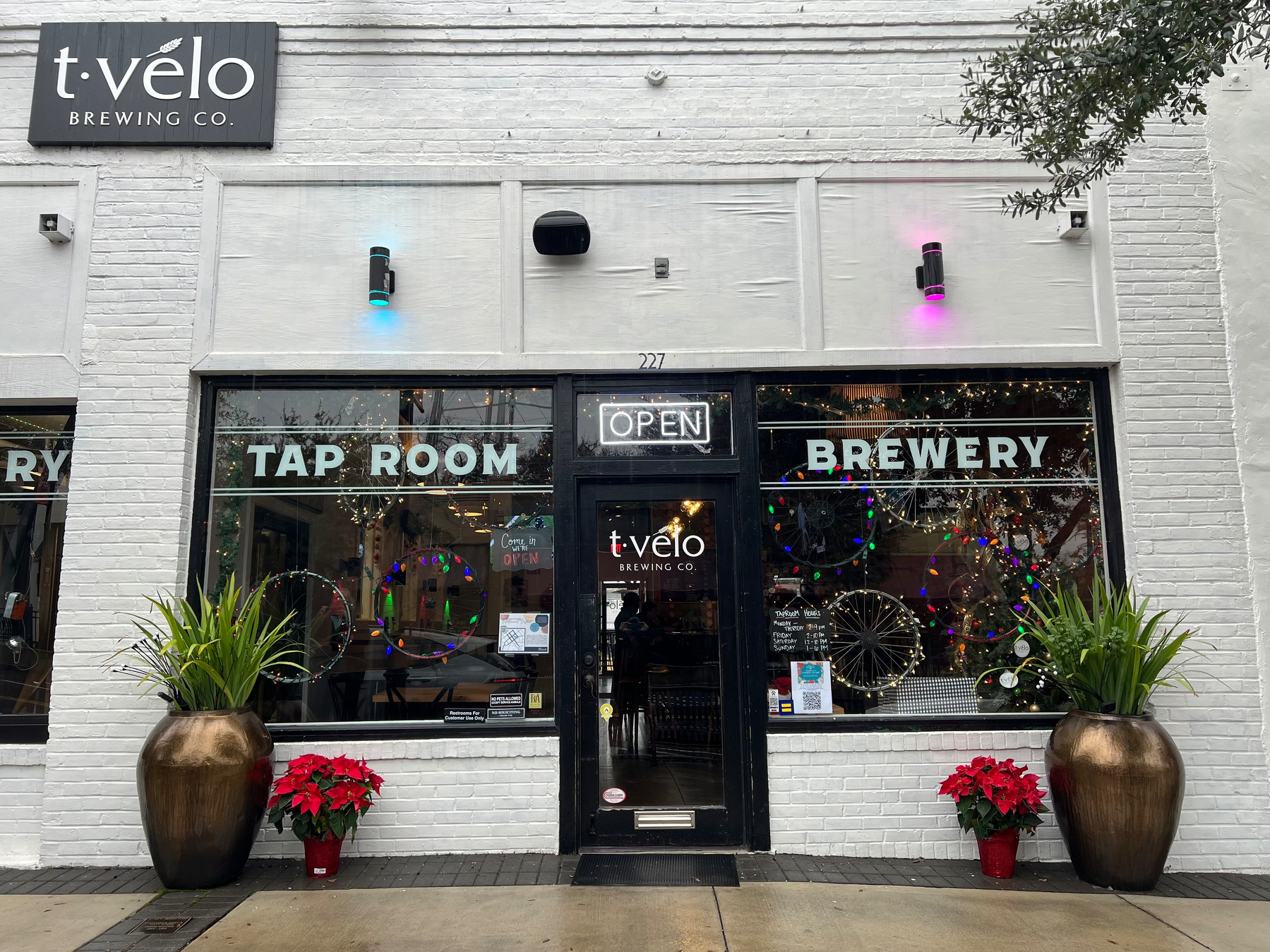 A brewery's entrance showcases Tap Room and Brewery signage, with decorative plants and festive lights.