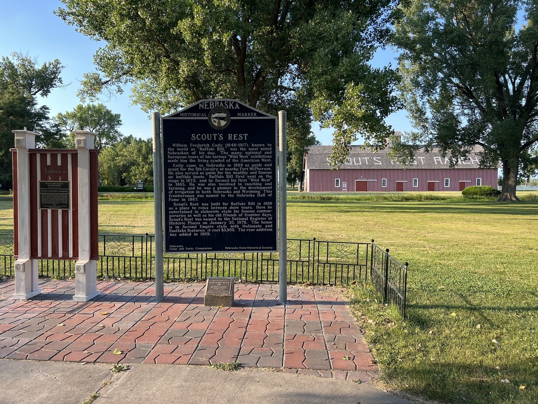 A historical marker in Nebraska details the significance of Scout's Rest, set against a background of trees and a red building labeled "Scout's Rest Ranch."