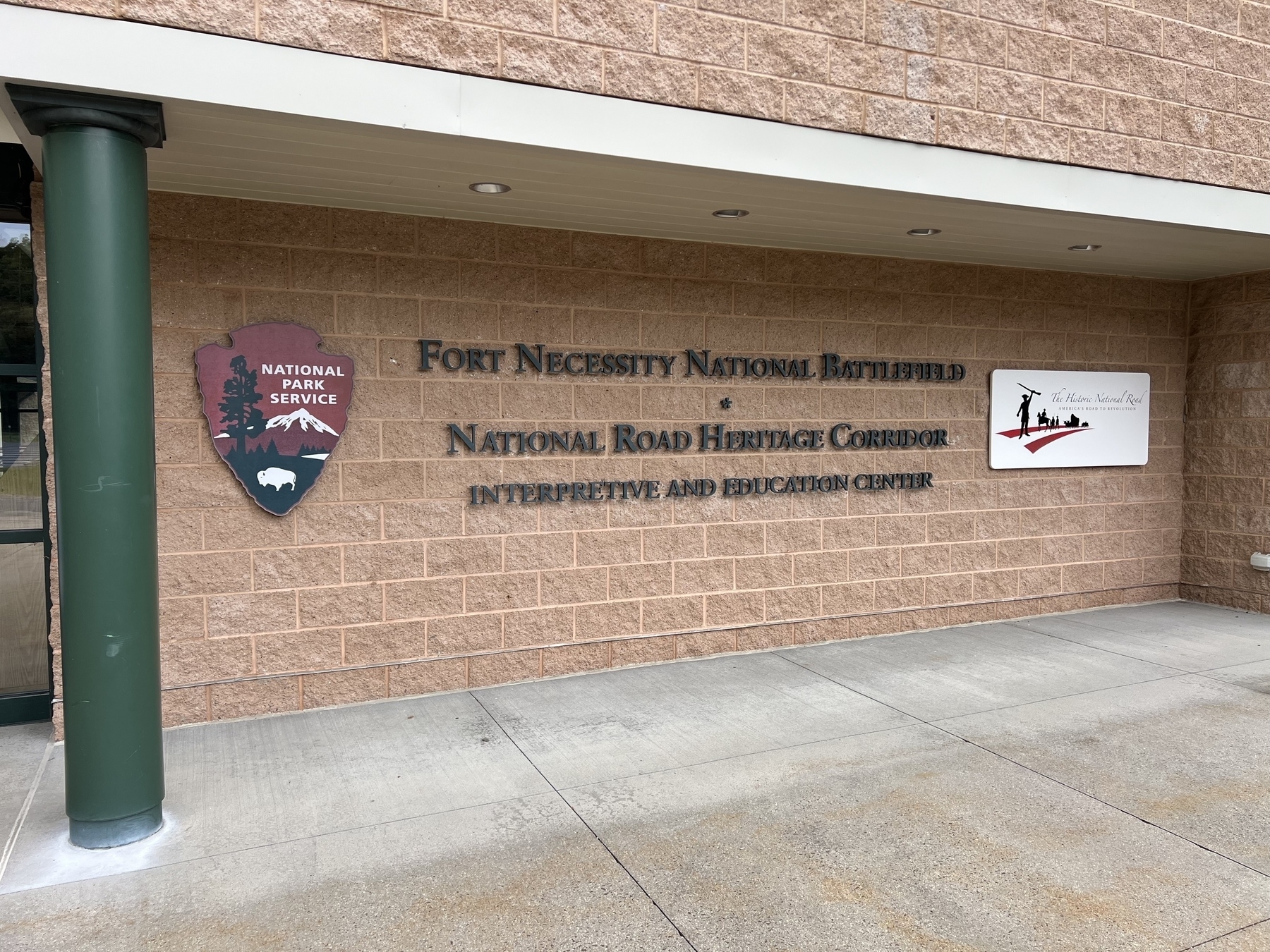 Fort Necessity National Battlefield's interpretive and education center is displayed with its logos on a brick building facade.